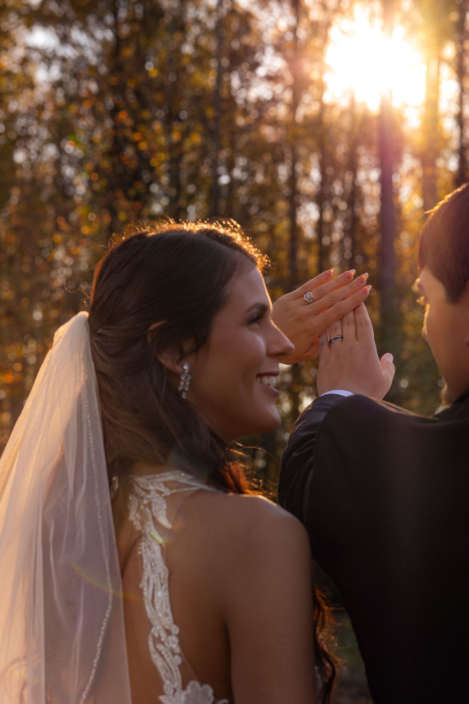 A bride and groom share a joyful moment at sunset with golden light filtering through autumn trees.