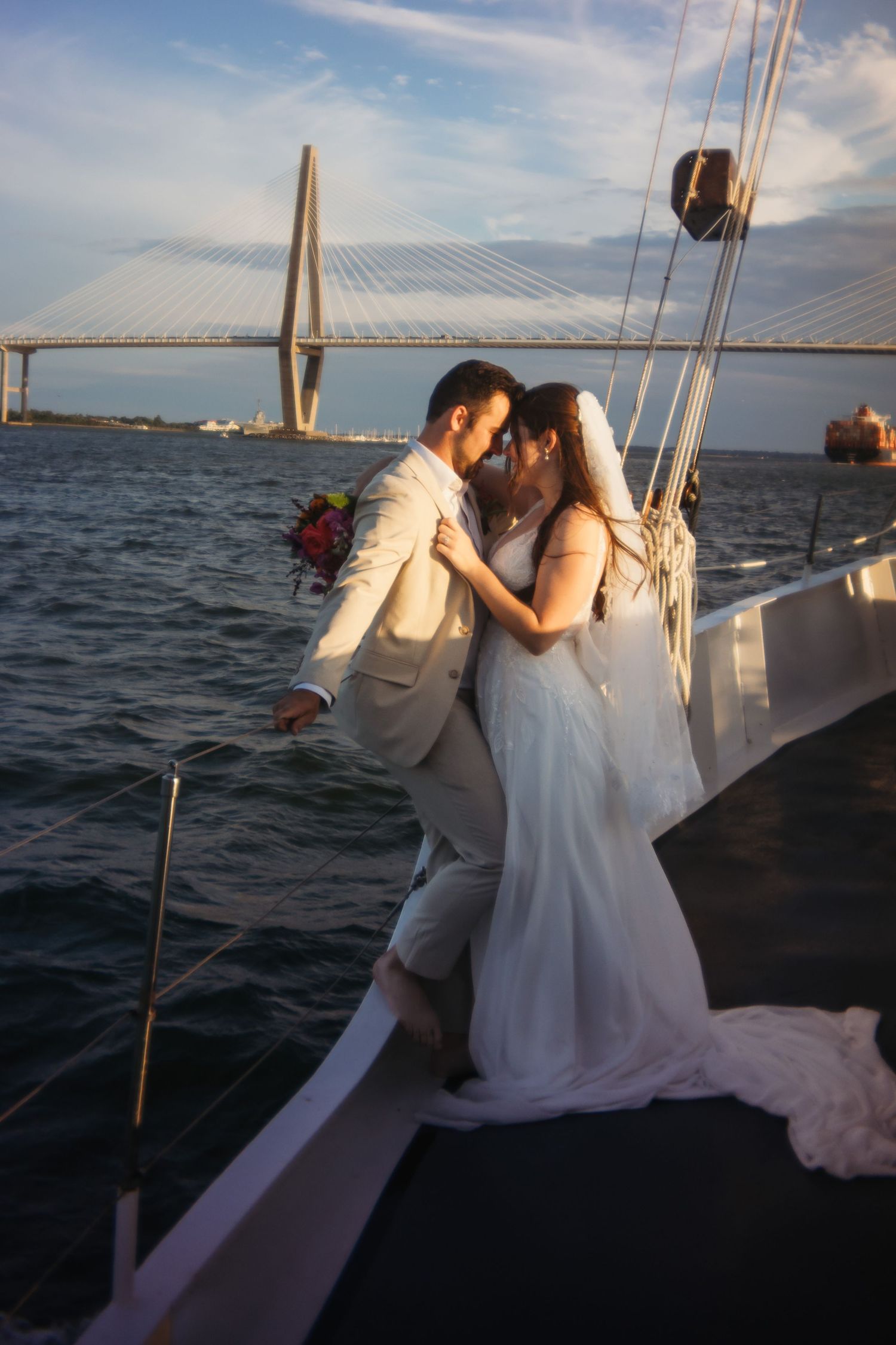 Romantic sunset sailing scene with couple in wedding attire on a boat near a bridge.