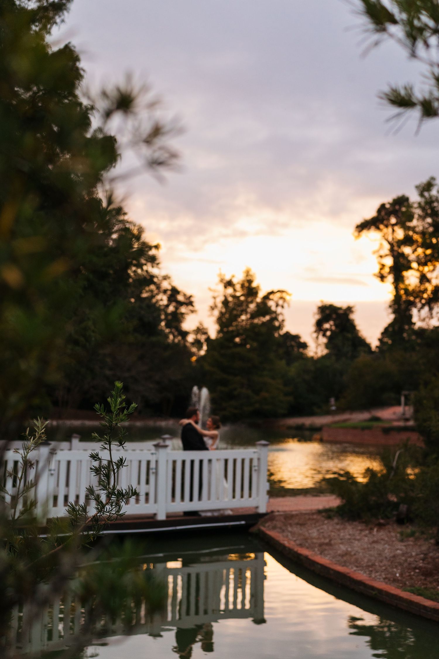 Scenic lakeside pathway with white picket fence and sunset reflecting on calm waters at dusk.