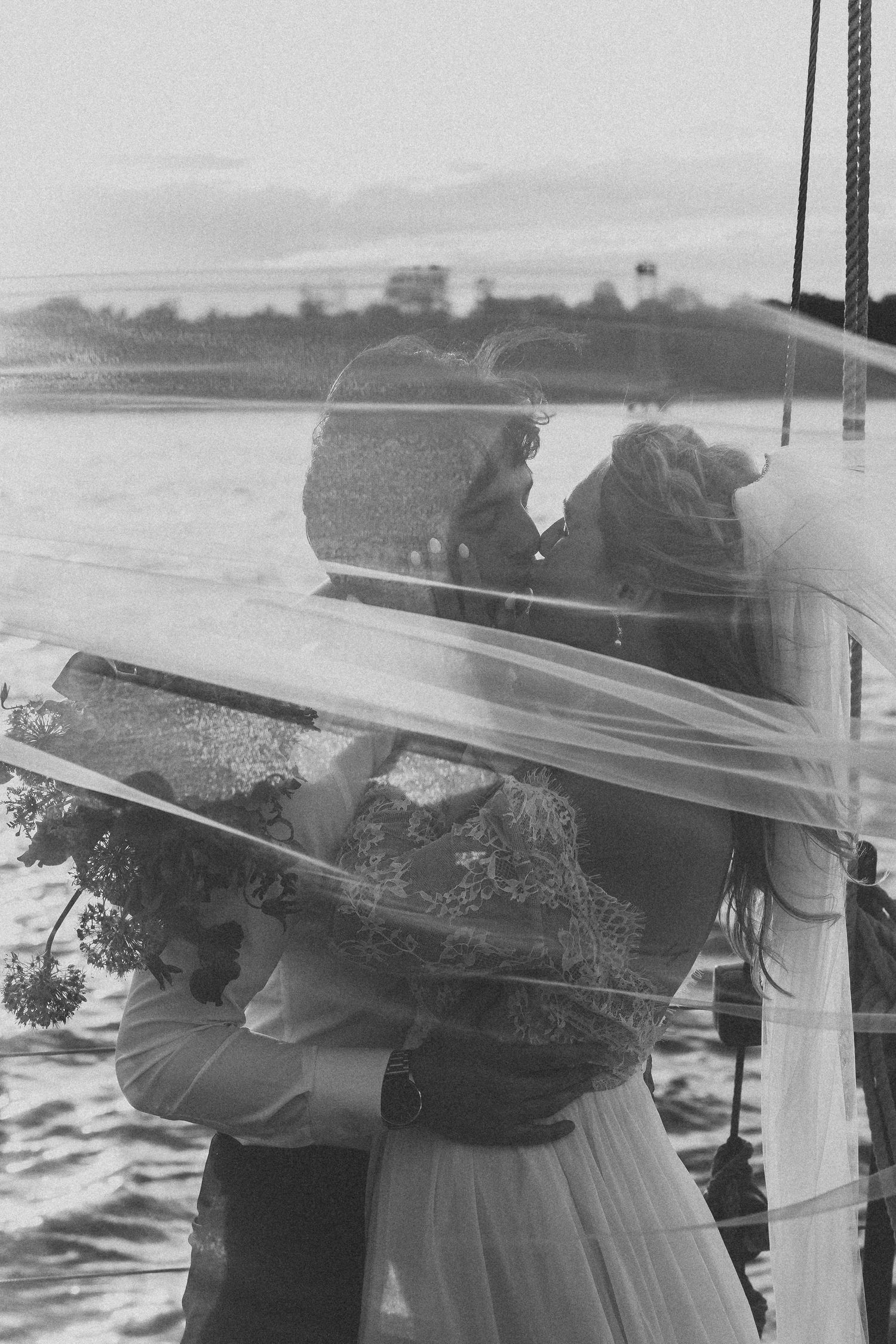 Artistic black and white photo of couple embracing on sailboat during sunset.