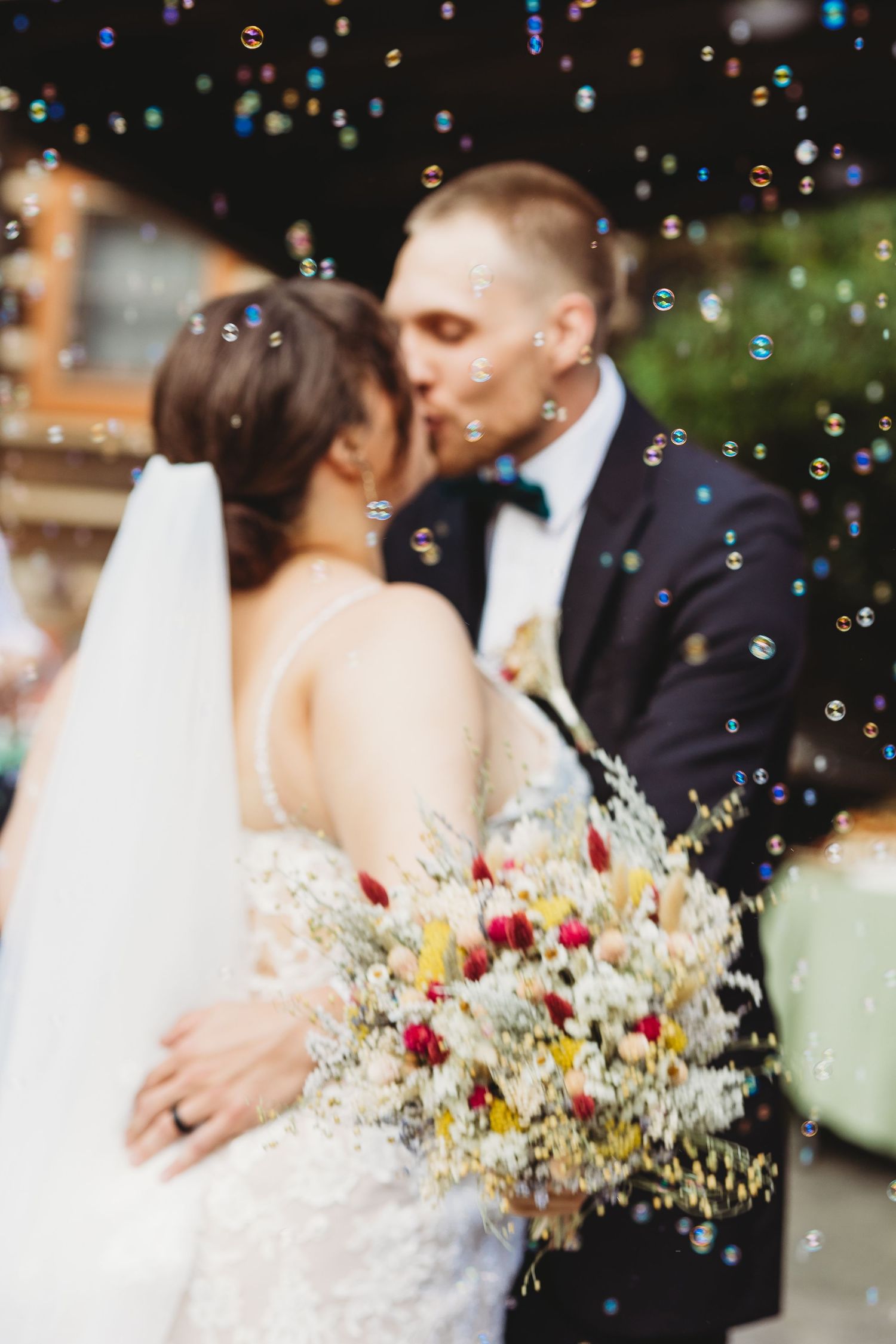 Romantic wedding couple embraces while delicate soap bubbles float around them with a dreamy outdoor backdrop.