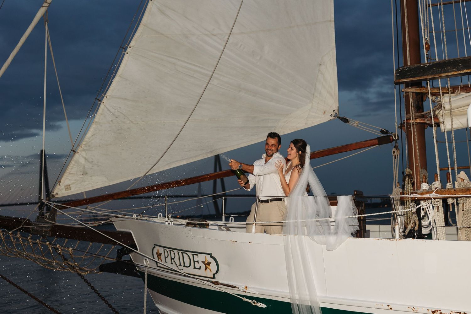 White sailboat with wedding couple aboard against blue ocean backdrop.