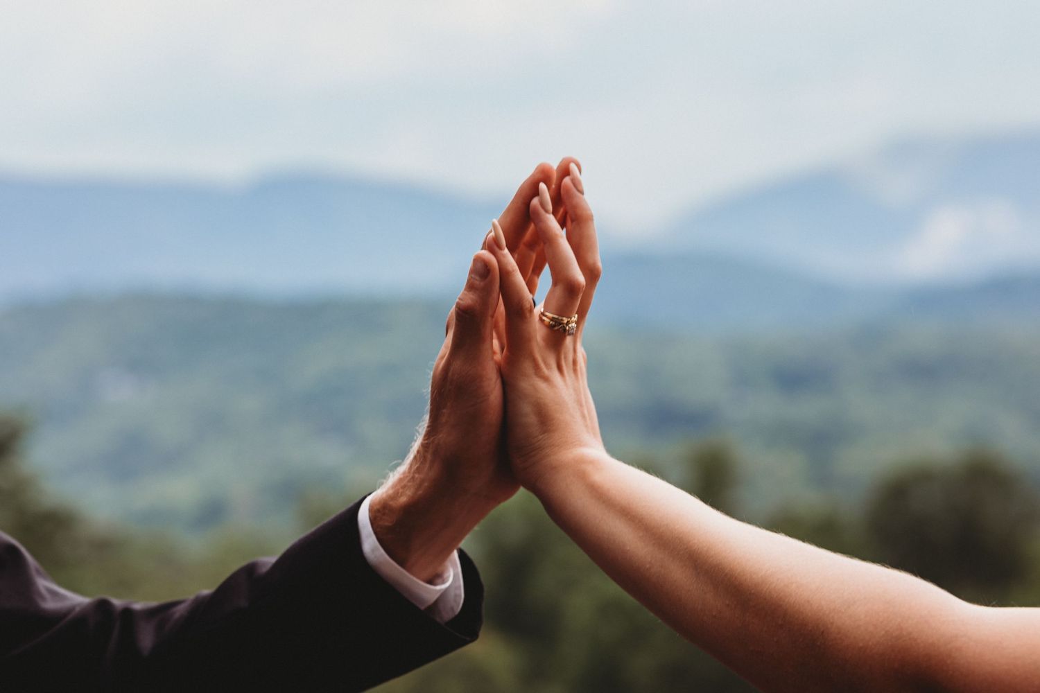 People joining hands together in a circle against a scenic mountain landscape backdrop, symbolizing unity and teamwork.