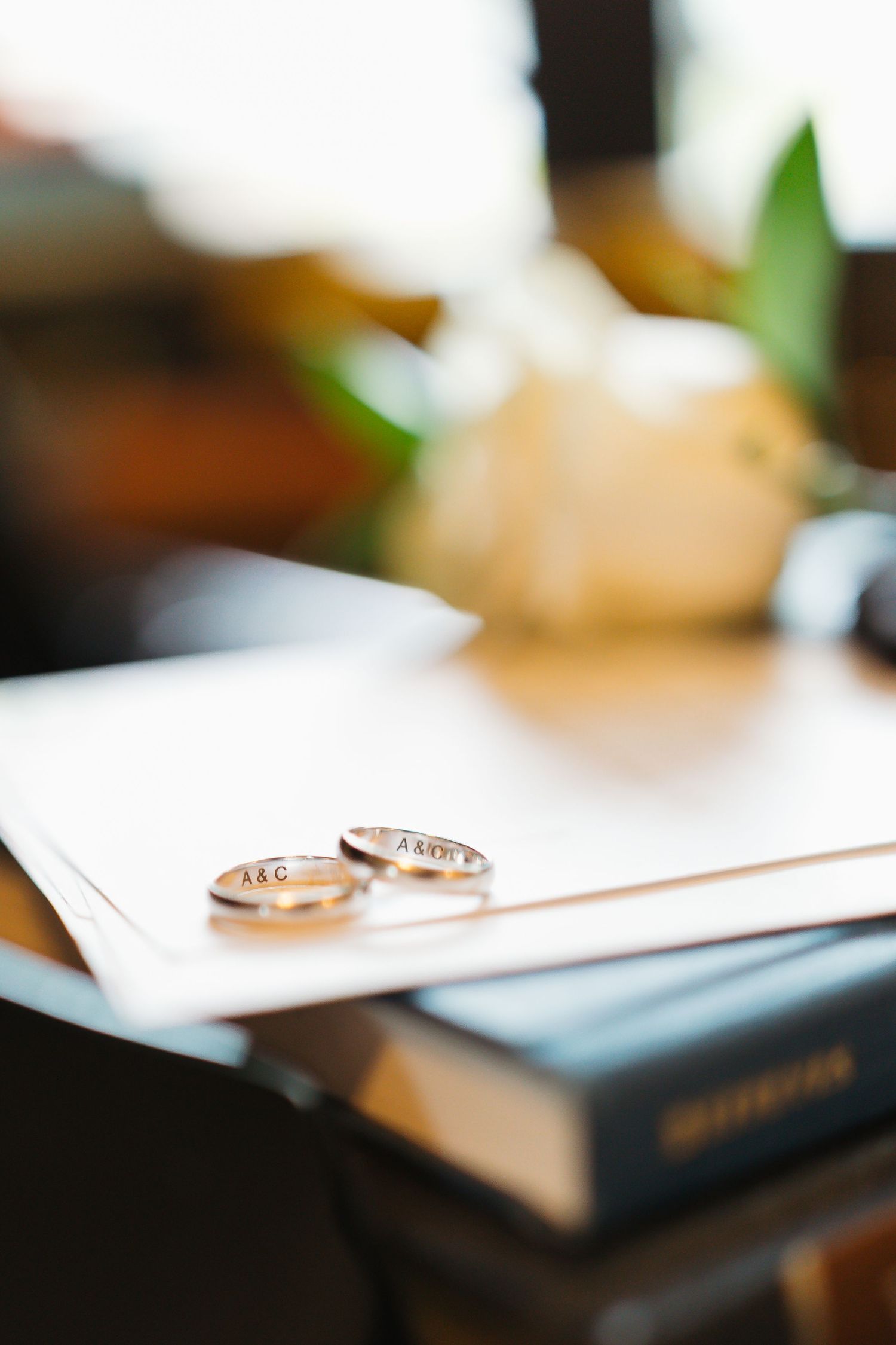 Two gold wedding rings rest on a white surface with a blurred background and soft lighting.