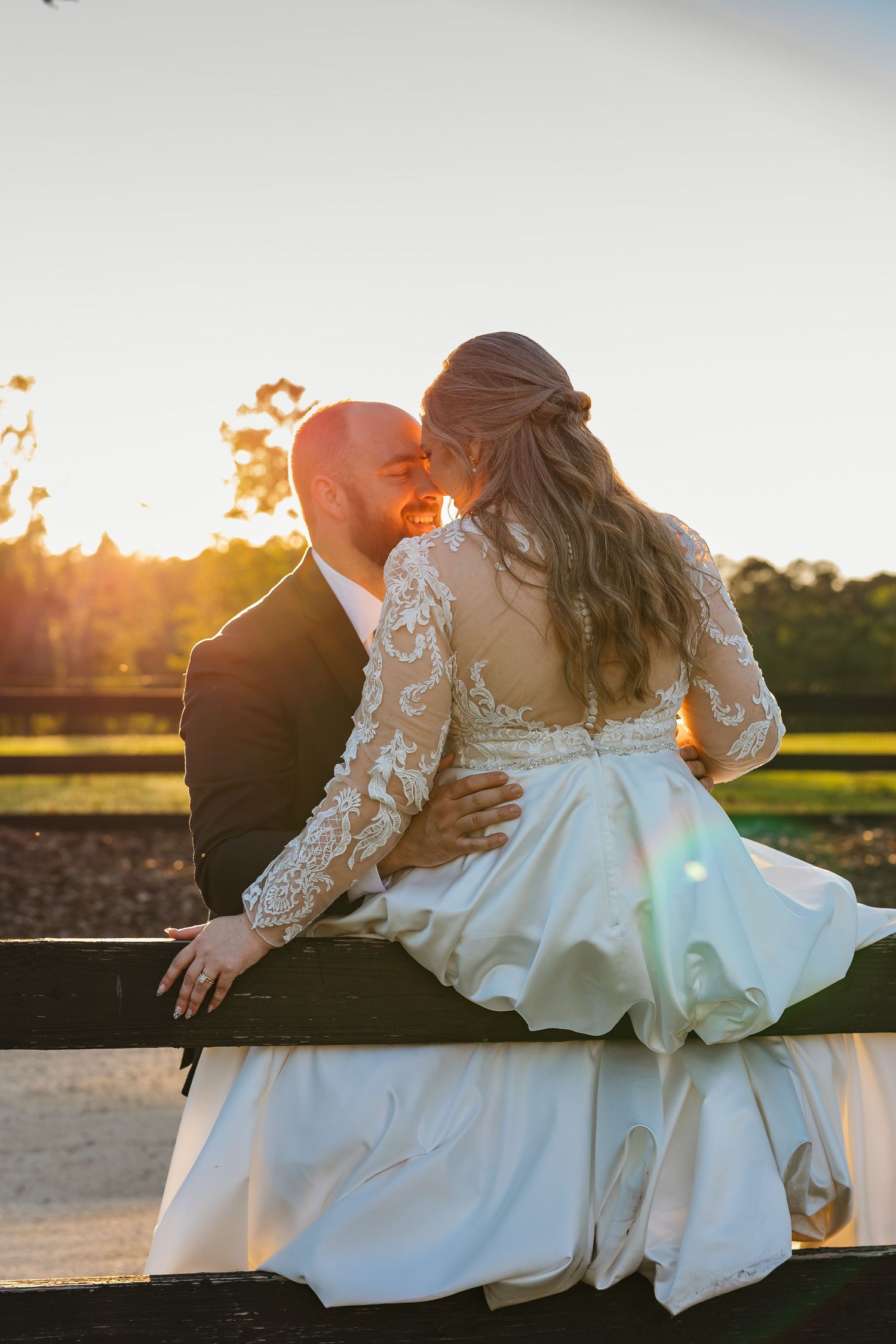 Romantic wedding couple embraces during golden hour sunset in an outdoor setting with flowing white dress.