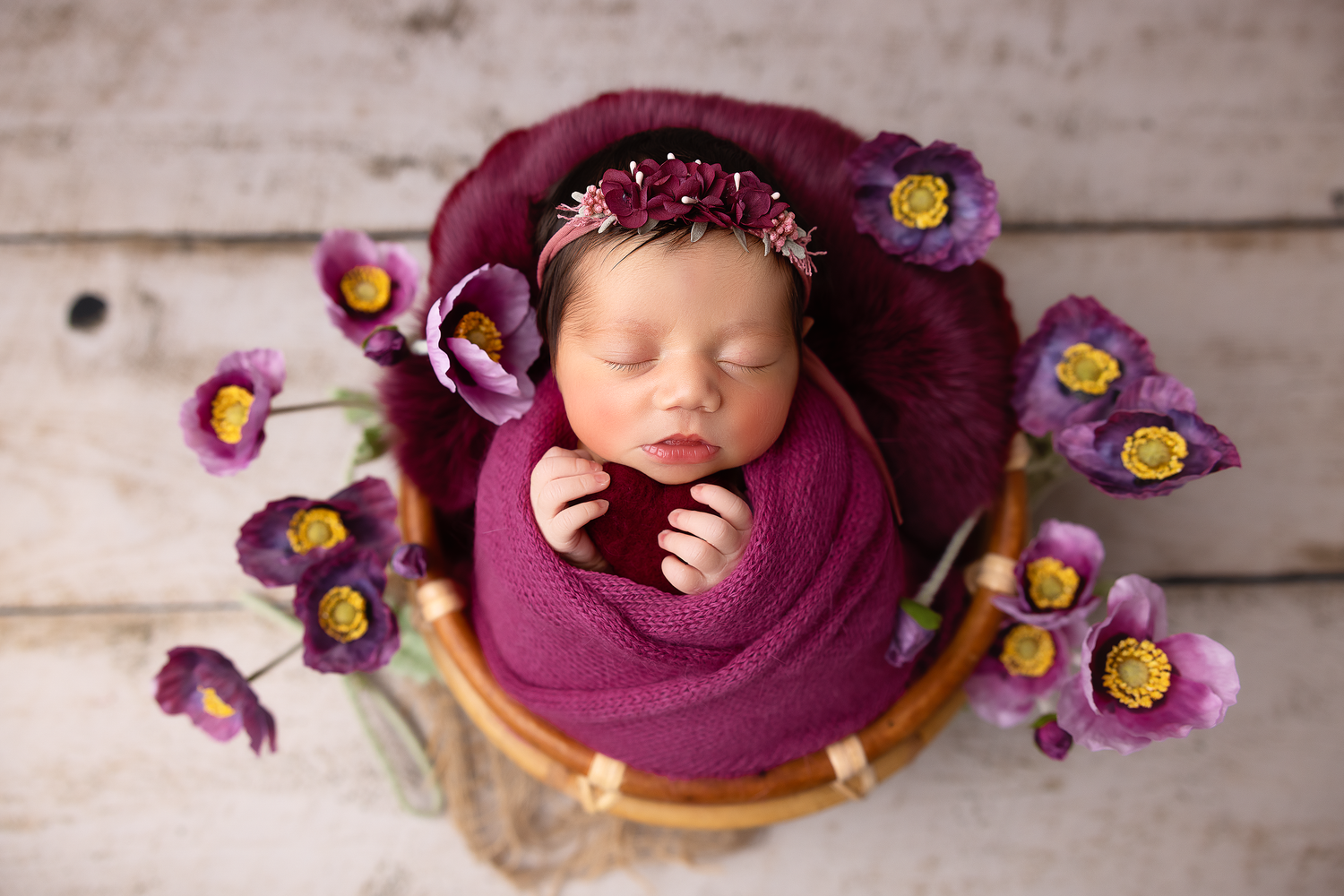 Artistic newborn portraits with purple flowers on wooden background.