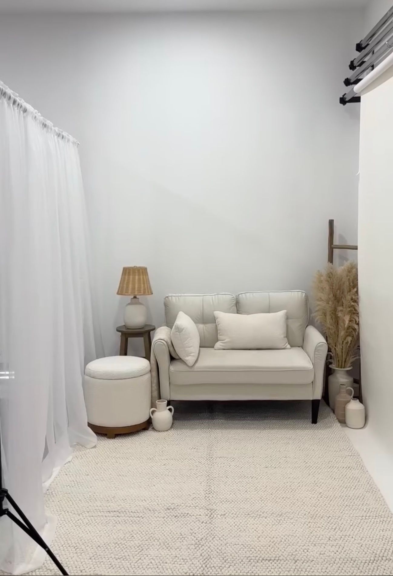 A minimalist photography studio space with white walls, beige couch, and textured carpet creating a bright, clean aesthetic.