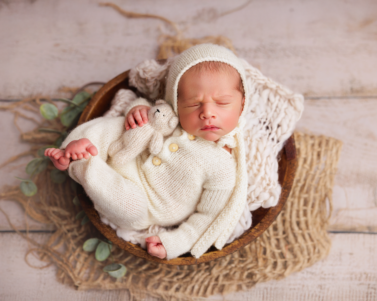 Newborn baby sleeping peacefully on textured burlap blanket wearing soft white knit wrap in rustic setting.