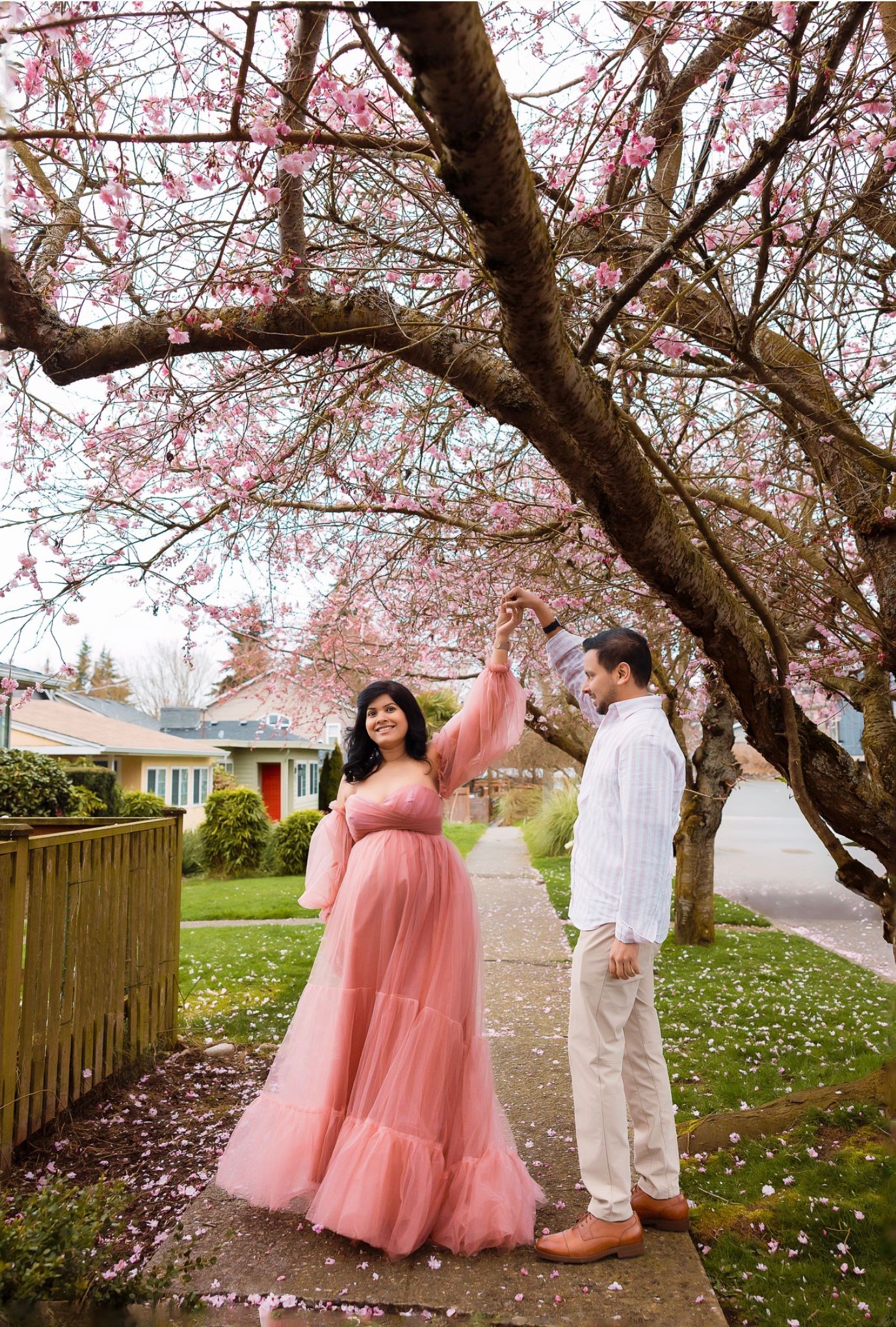 A romantic couple poses beneath blooming cherry blossom trees in a springtime photoshoot series.