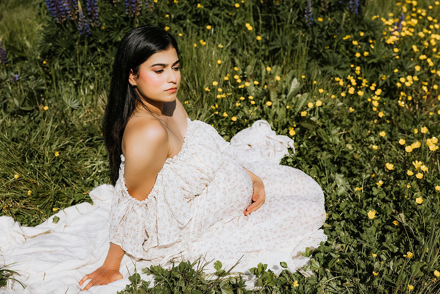 A bride in a flowing white lace gown poses gracefully in a garden filled with vibrant yellow wildflowers.
