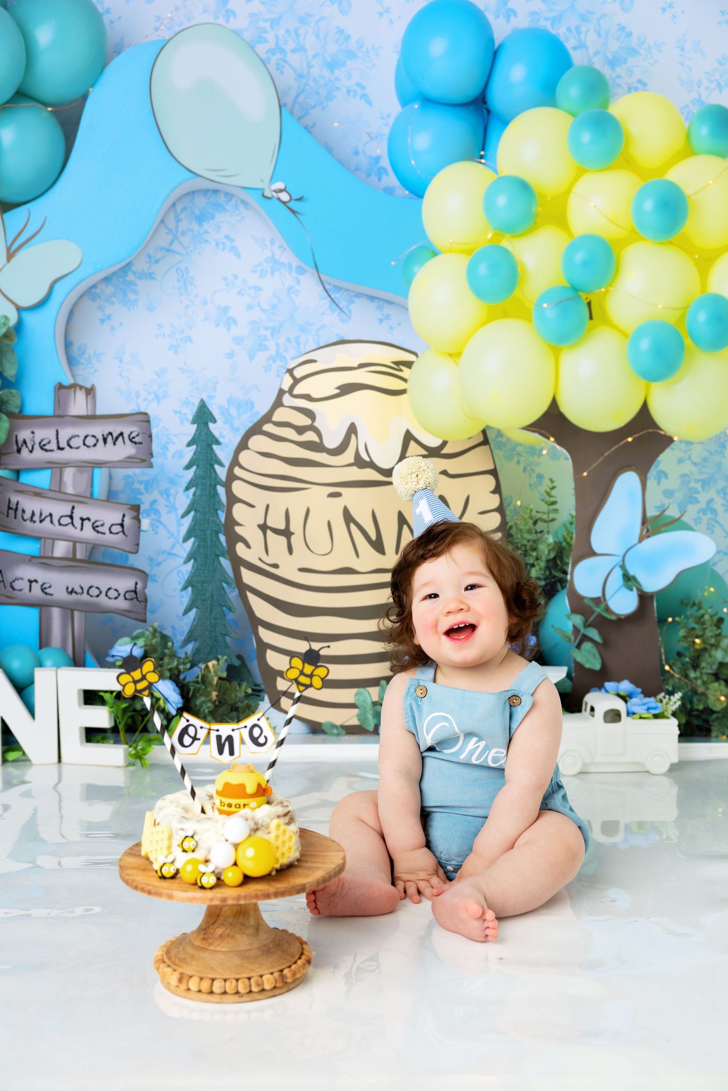 Baby's first birthday cake smash with Winnie the Pooh theme, balloons, and honey pot backdrop.