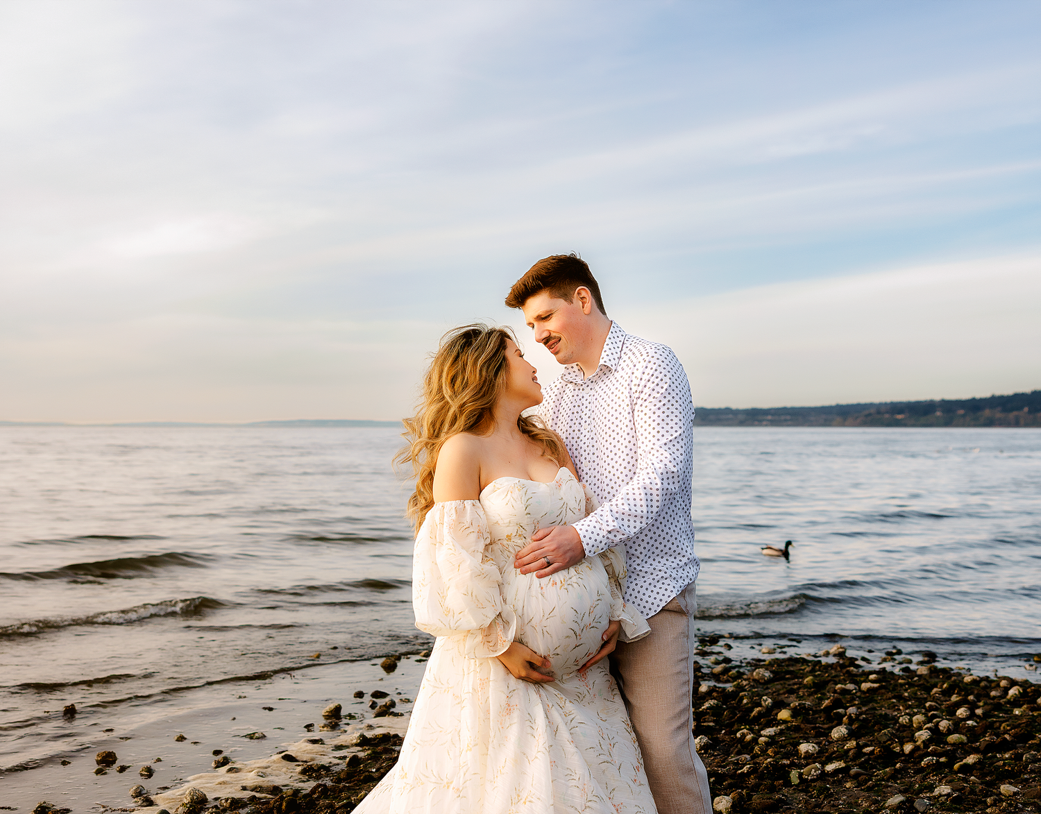 Newlywed couple embraces on a rocky beach at sunset with ocean waves in the background.