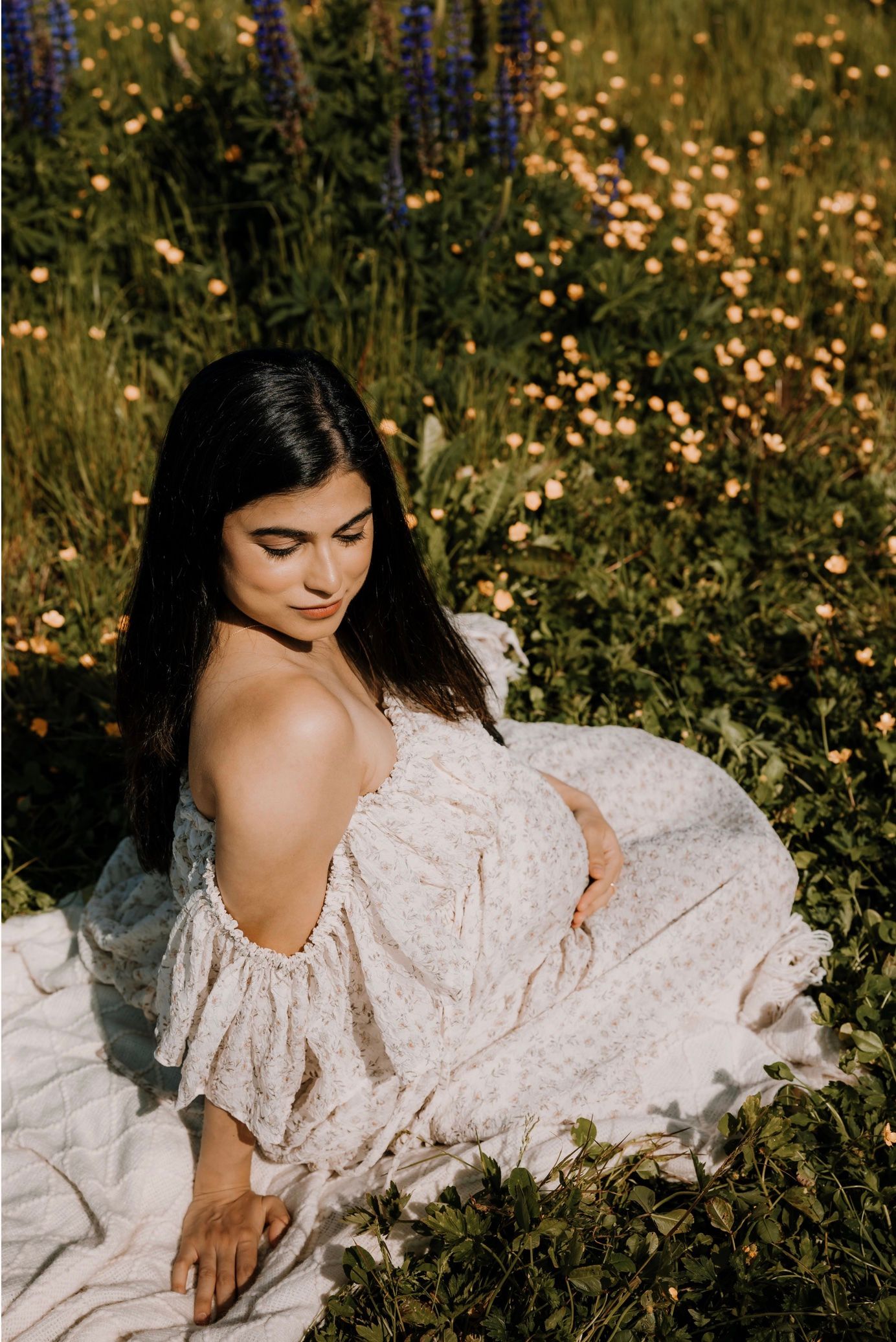 A person in a flowing white dress reclines among wildflowers in a dreamy outdoor setting during golden hour.