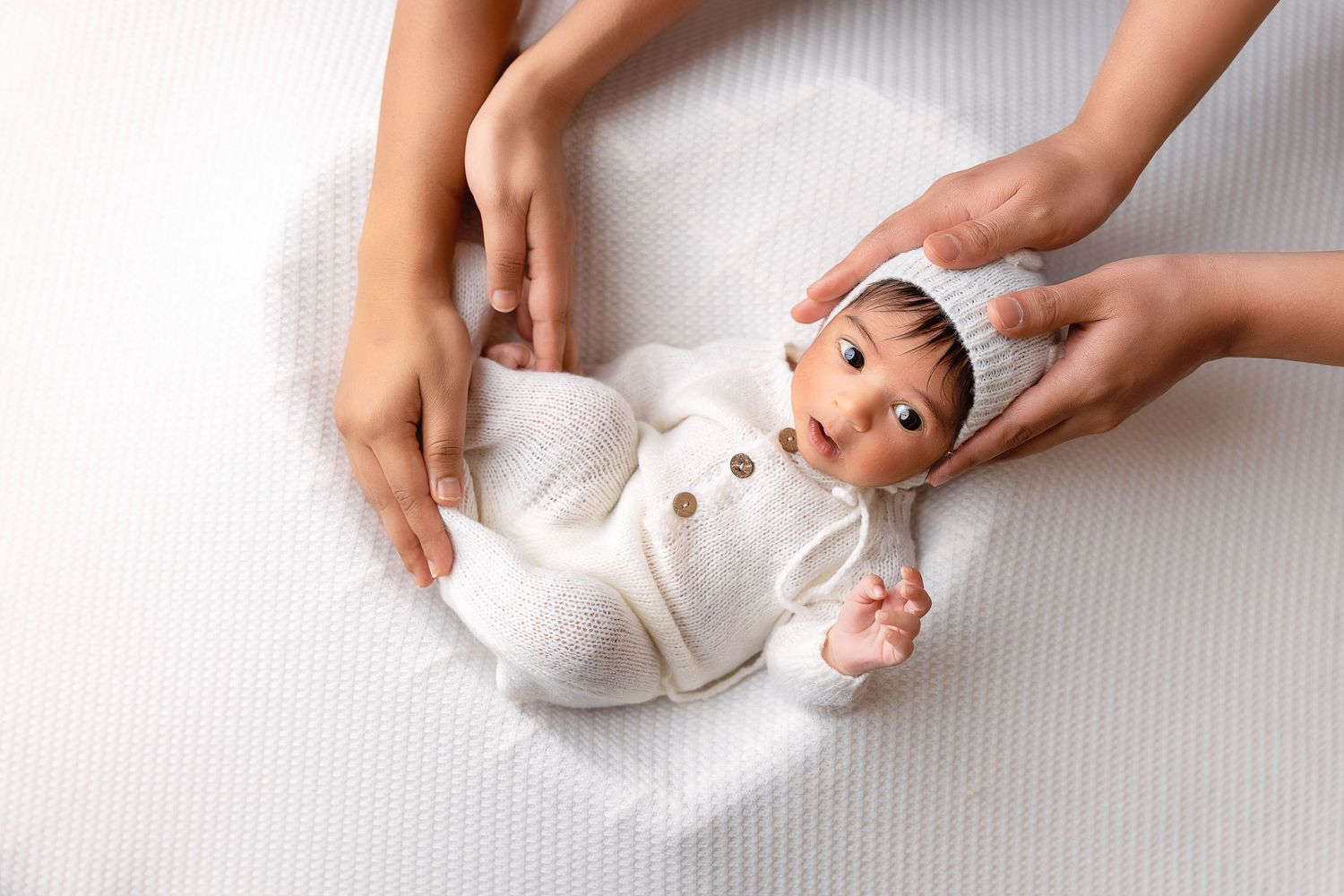 Wide-awake newborn baby resting in a heart-shaped bowl, gently held by mom and dad during a studio session