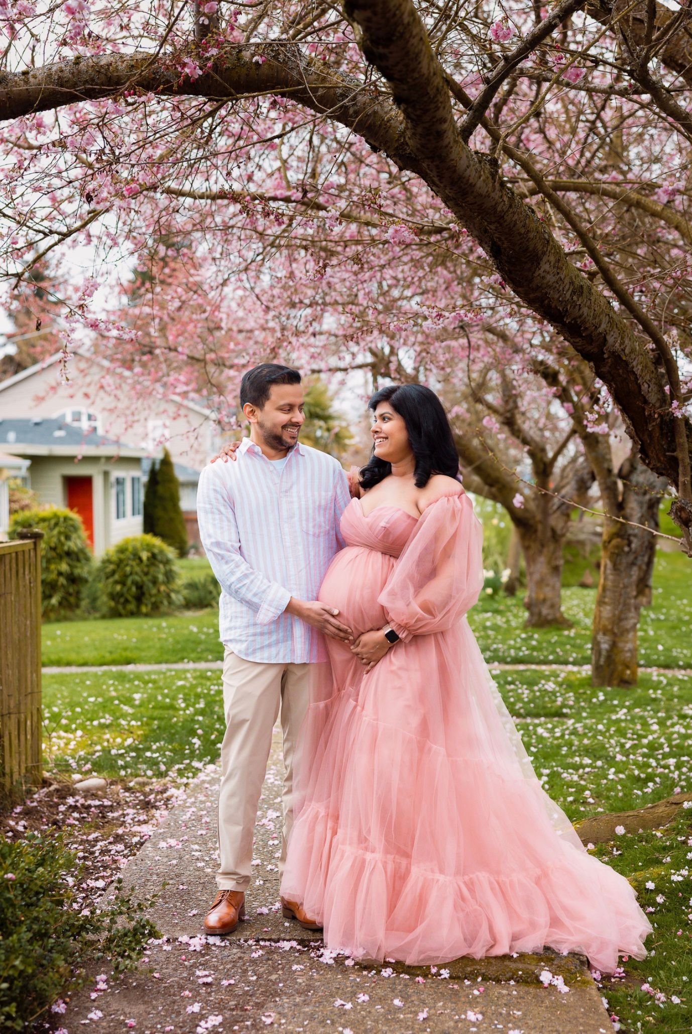 A romantic couple dances beneath blooming cherry blossom trees while pink petals fall around them in a springtime garden.