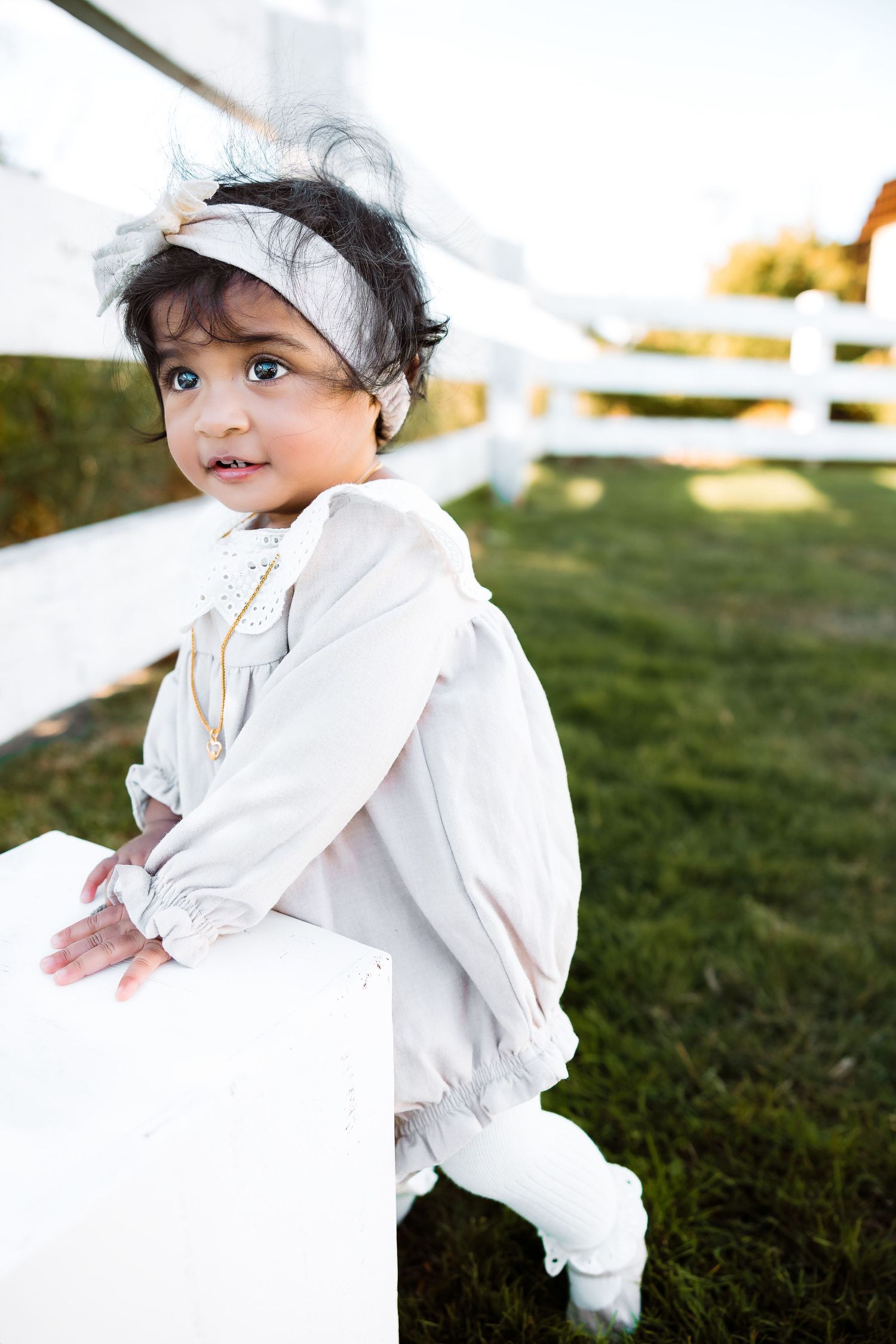 Baby in ruffled white dress crawls and plays on green grass outdoors.