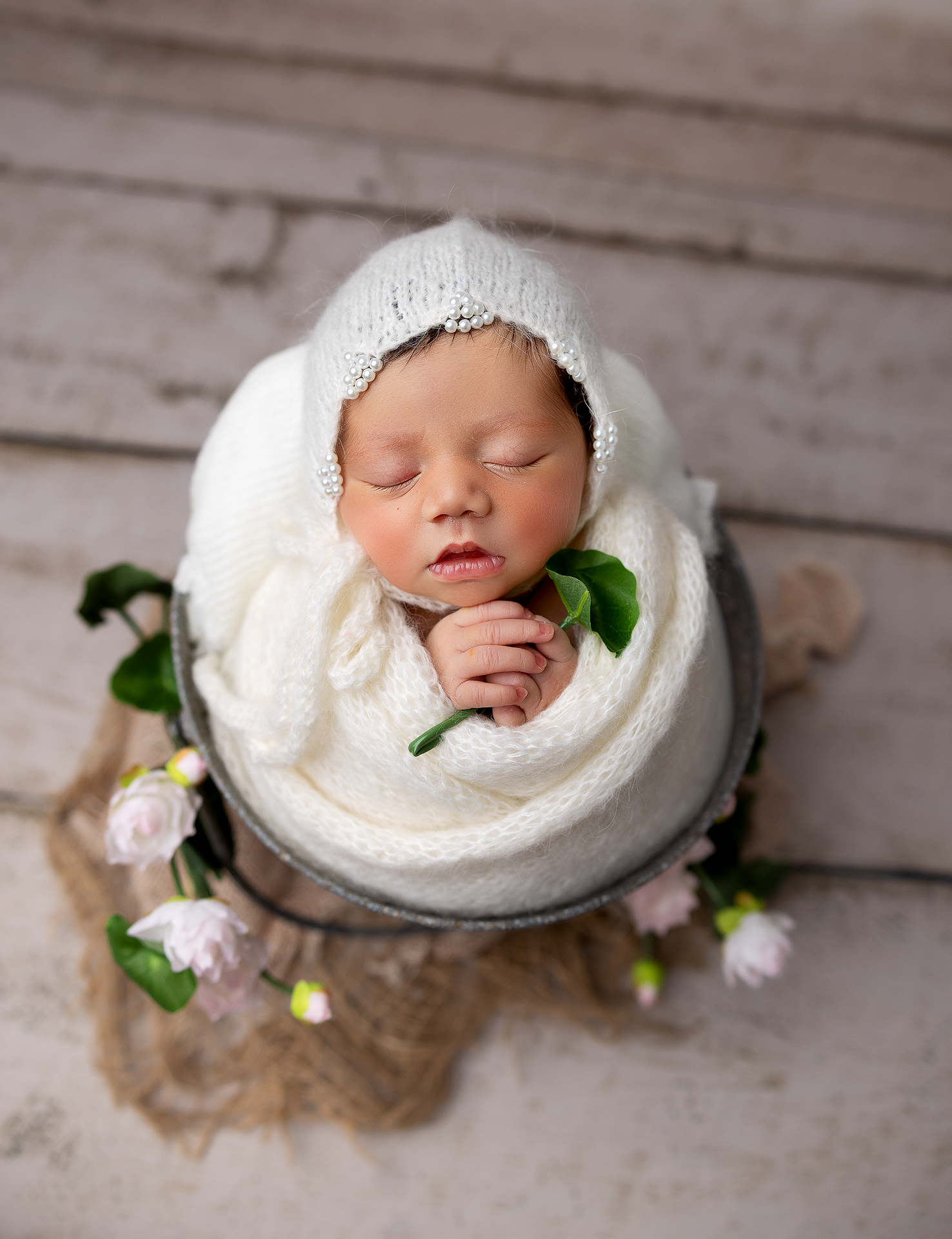 Newborn baby sleeping in white bowl with delicate floral accents.