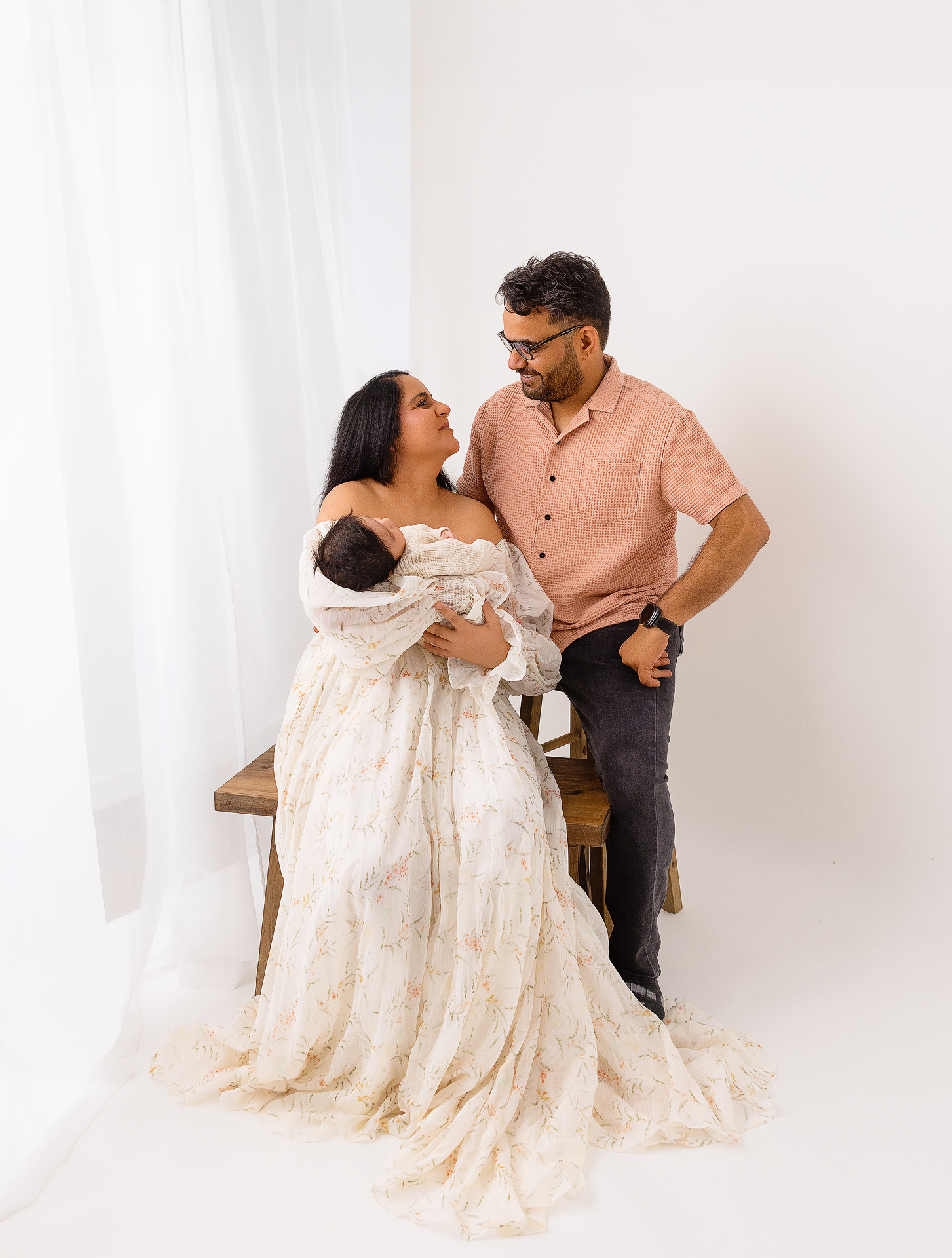 A couple in cream and peach outfits share intimate moments against a white backdrop during a photo session.