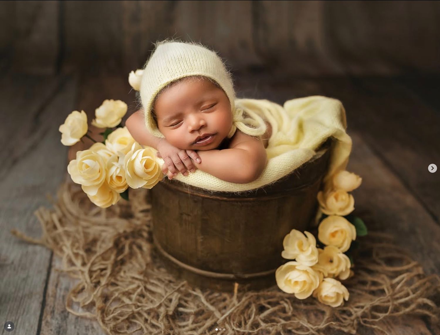 Sleeping newborn baby nestled in a wooden bucket prop surrounded by delicate yellow roses  during seattle newborn photography session
