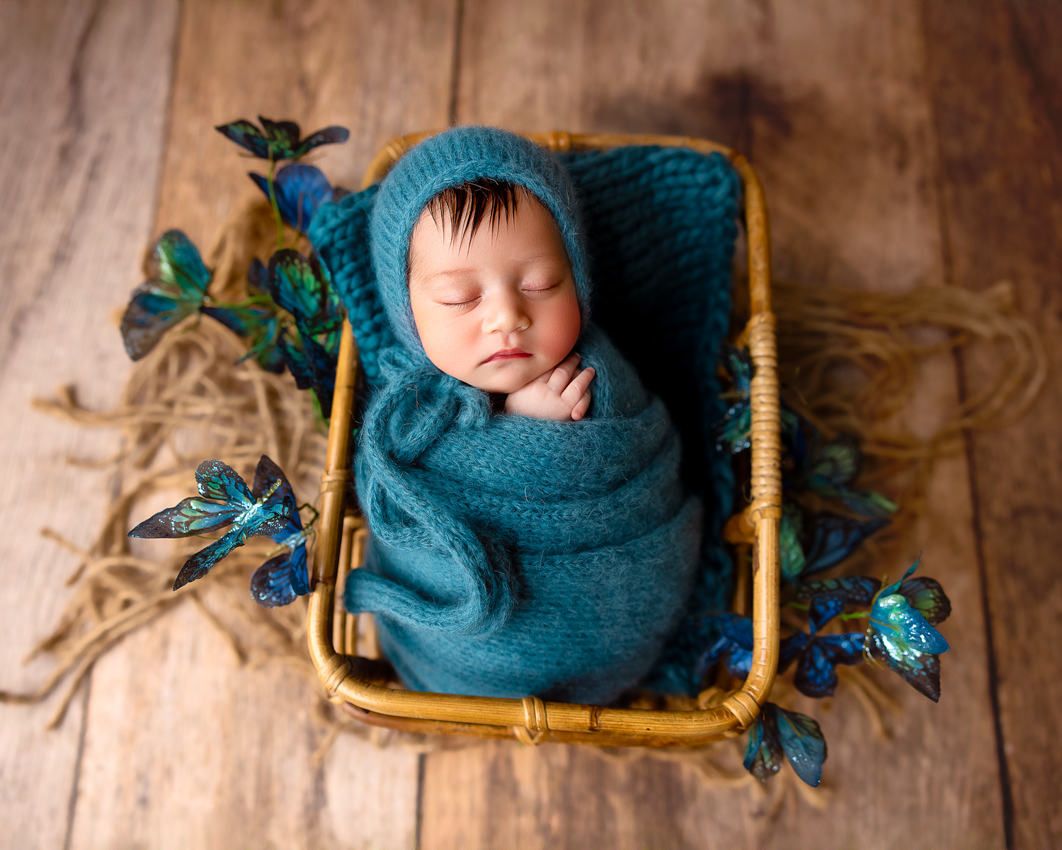 Newborn baby wrapped in teal blanket sleeping peacefully on wooden backdrop with rustic props.