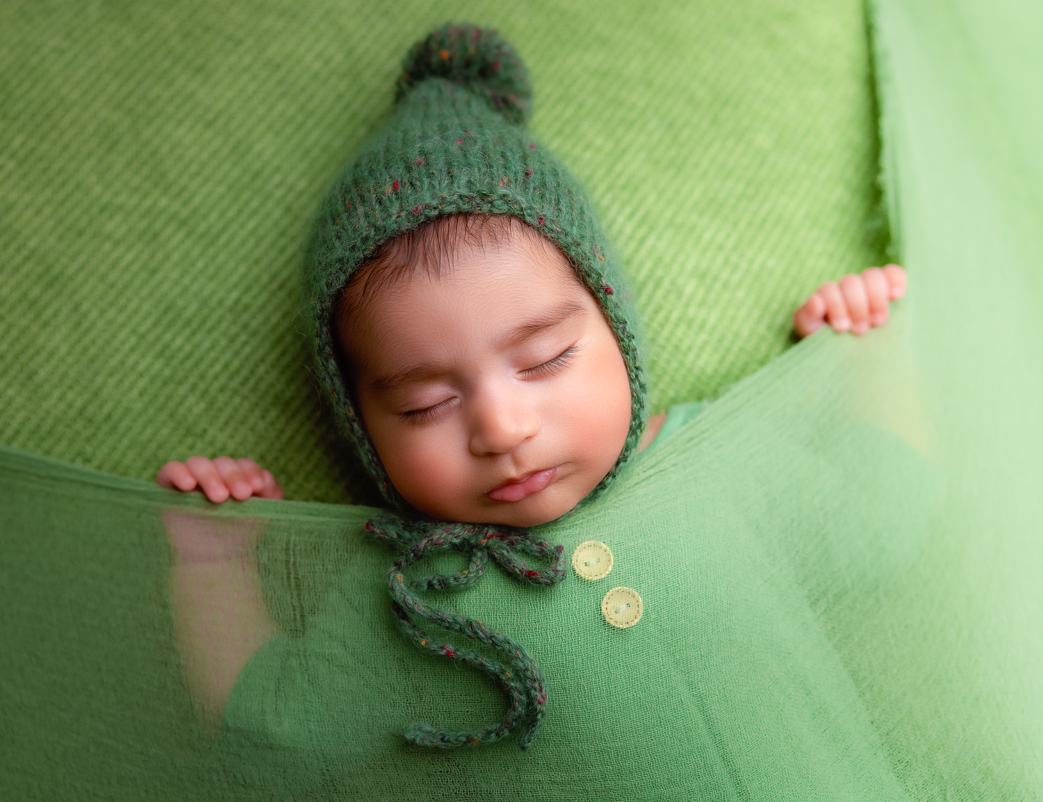 Sweet newborn portraits with green knit accessories against matching background.