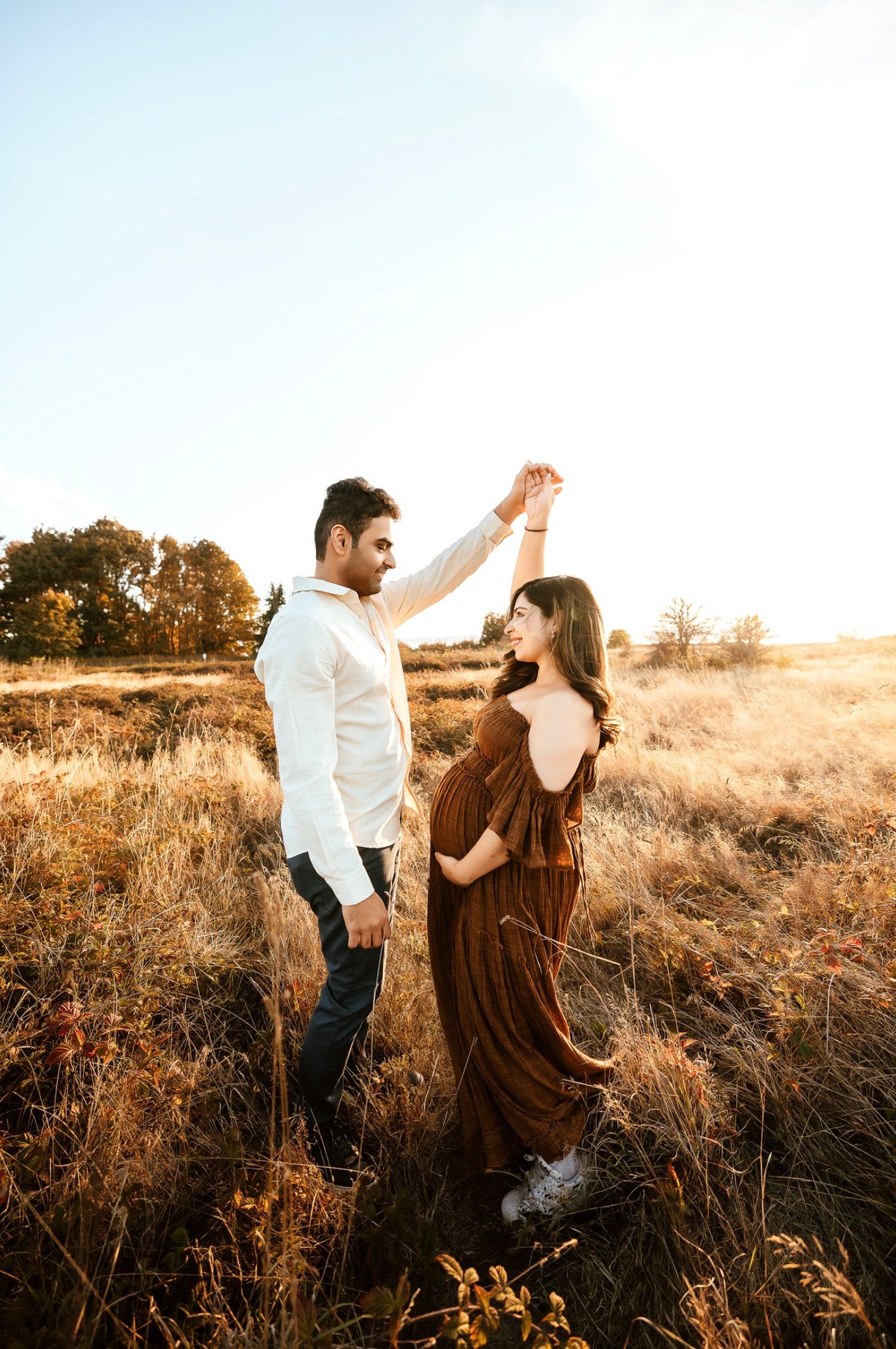 A couple dances together in a golden field at sunset, creating a romantic silhouette against the warm evening light.