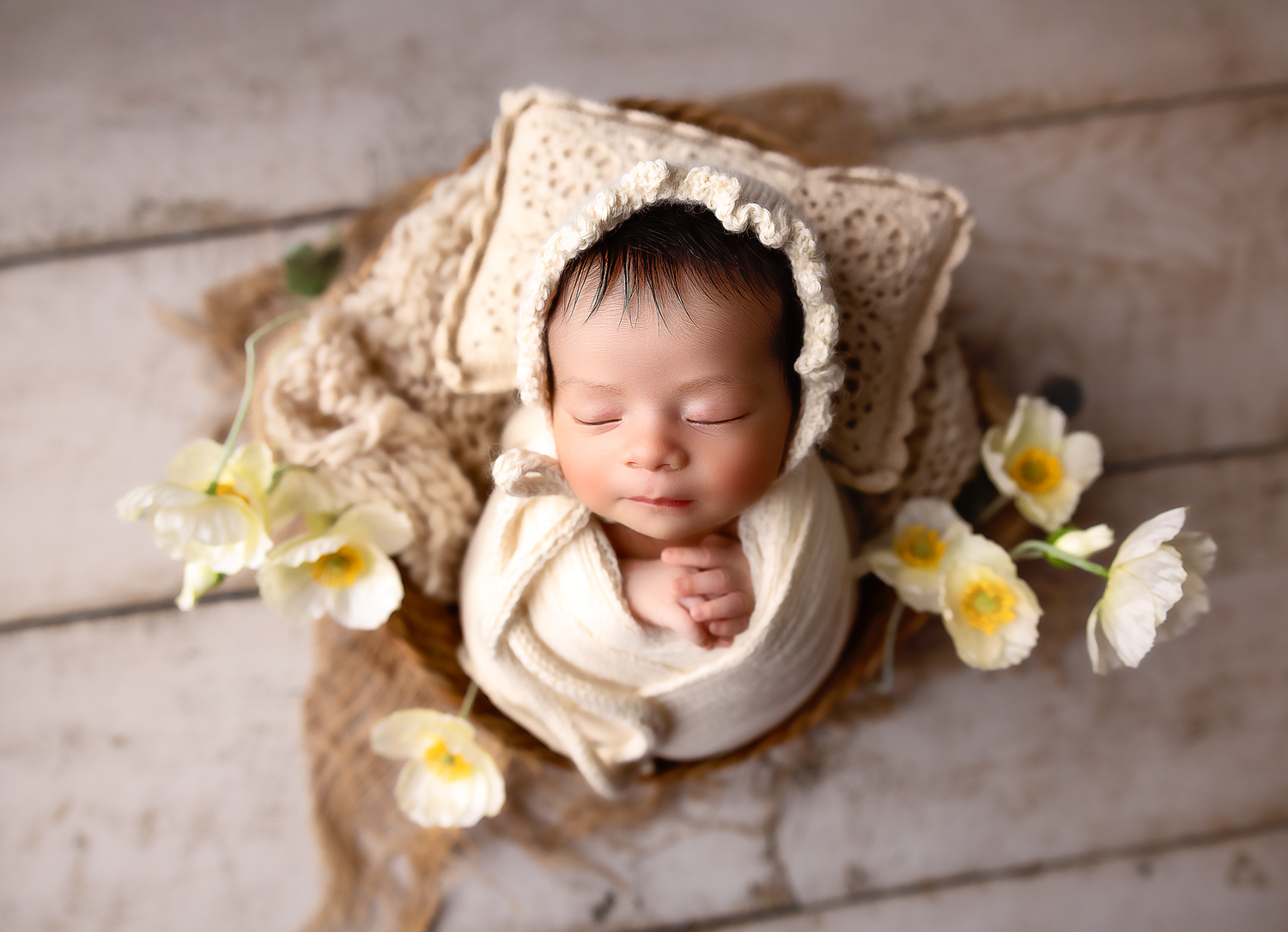 Delicate newborn photography with white daisies on rustic wooden backdrop.