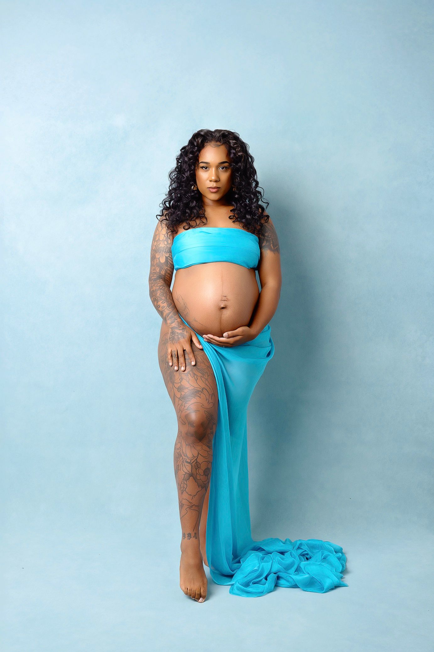Maternity photo series showing an expectant mother in turquoise fabric against a light blue backdrop.
