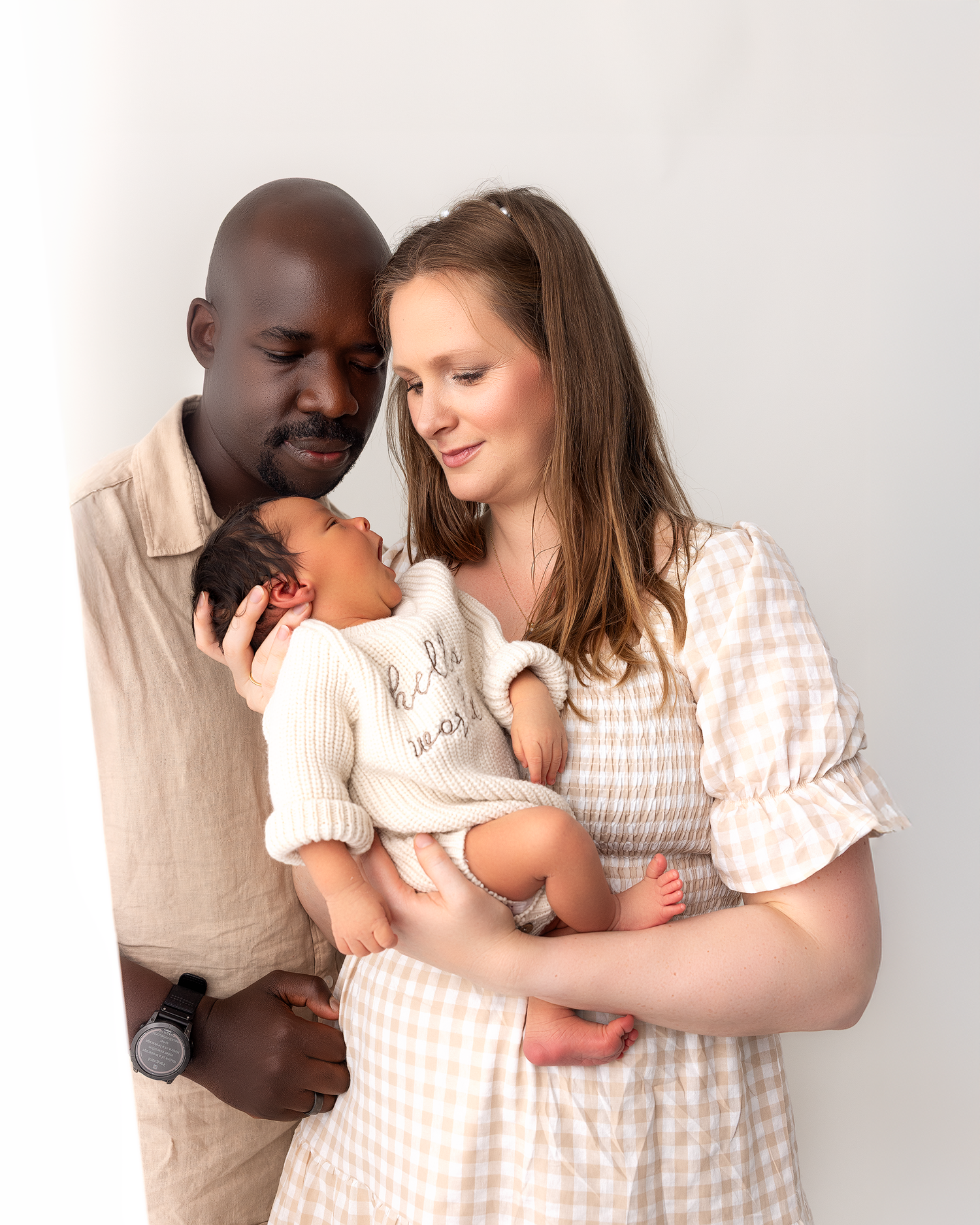 A family in coordinating neutral outfits shares tender moments in a minimalist everett studio setting.