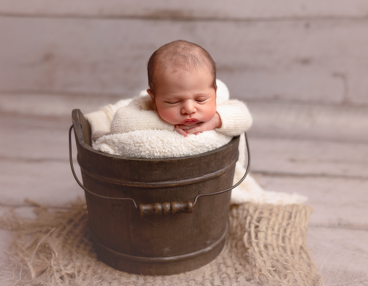A series of seven newborn baby photos showing a sleeping infant nestled in rustic metal buckets with soft blankets.