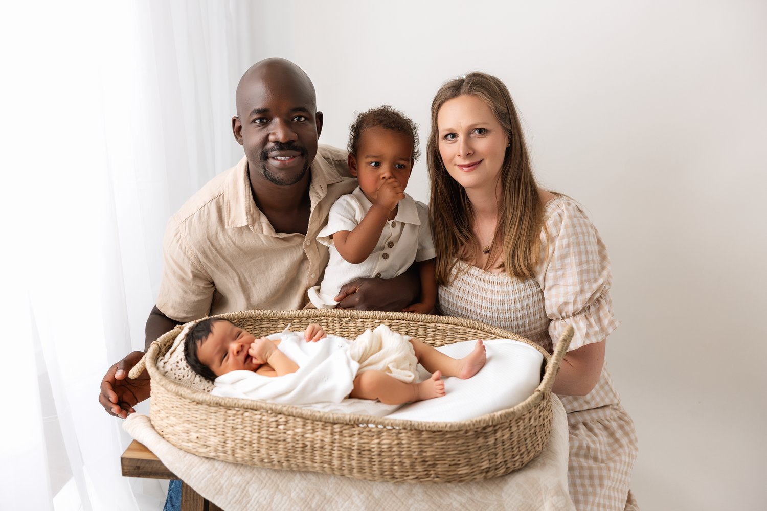 A family sits together with their newborn baby in a woven bassinet against a white backdrop Everett.