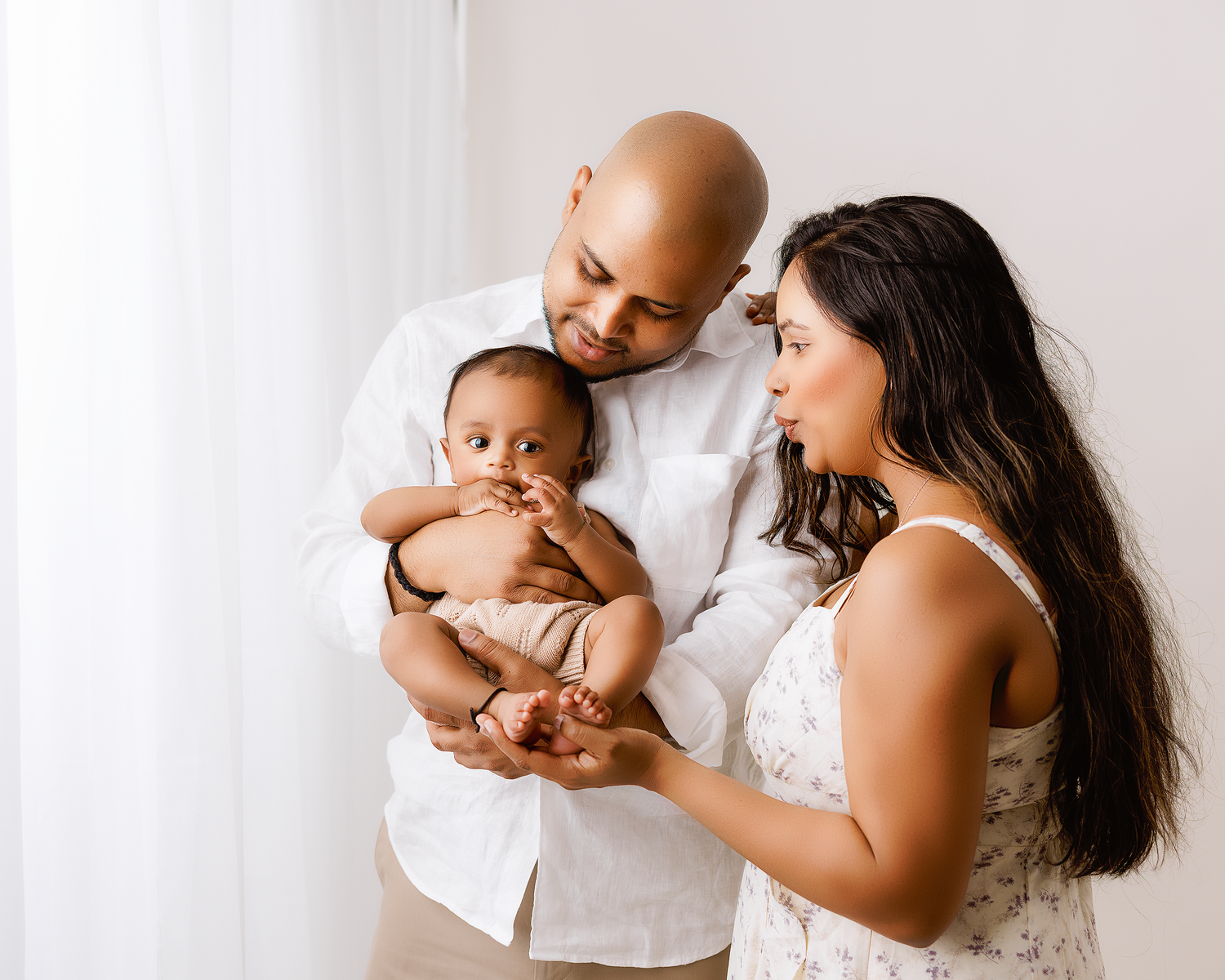 A series of four intimate newborn photography poses with parents in white against a light backdrop.