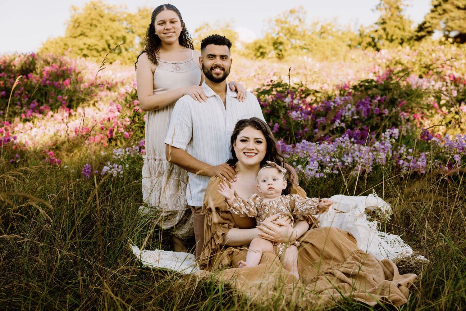 A couple sits together on a blanket in a field of vibrant wildflowers during golden hour.