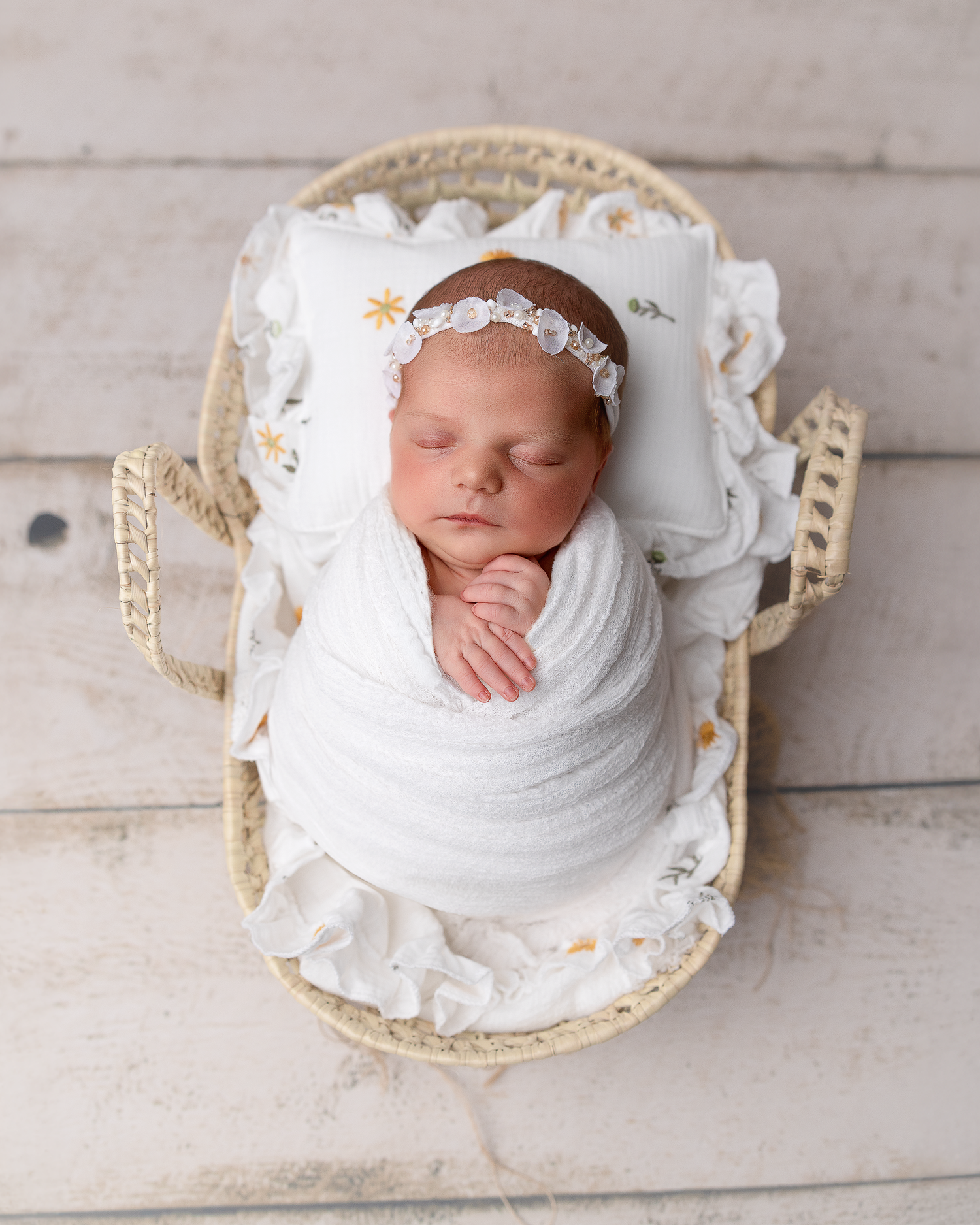 Sleeping newborn swaddled in white fabric rests peacefully in vintage-style cream colored decorative frames.