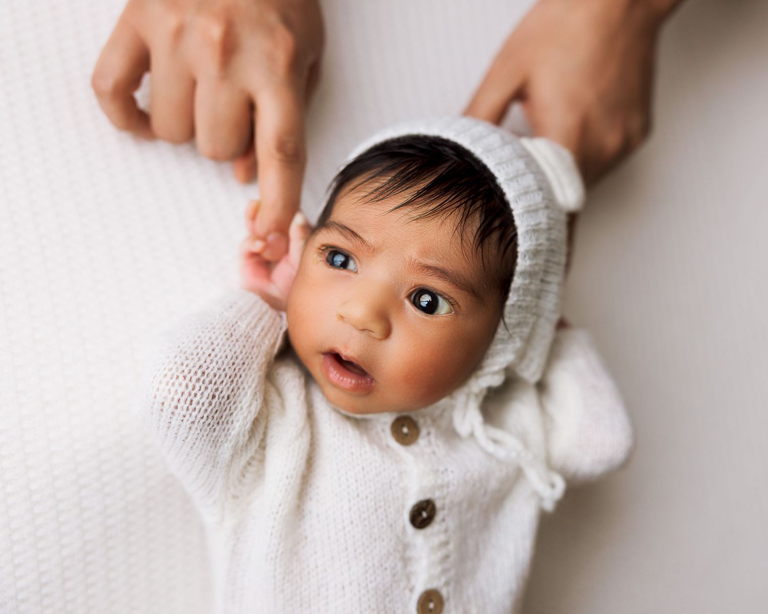 Baby wearing white knit sweater with wooden buttons looks to the side in close-up portrait series.