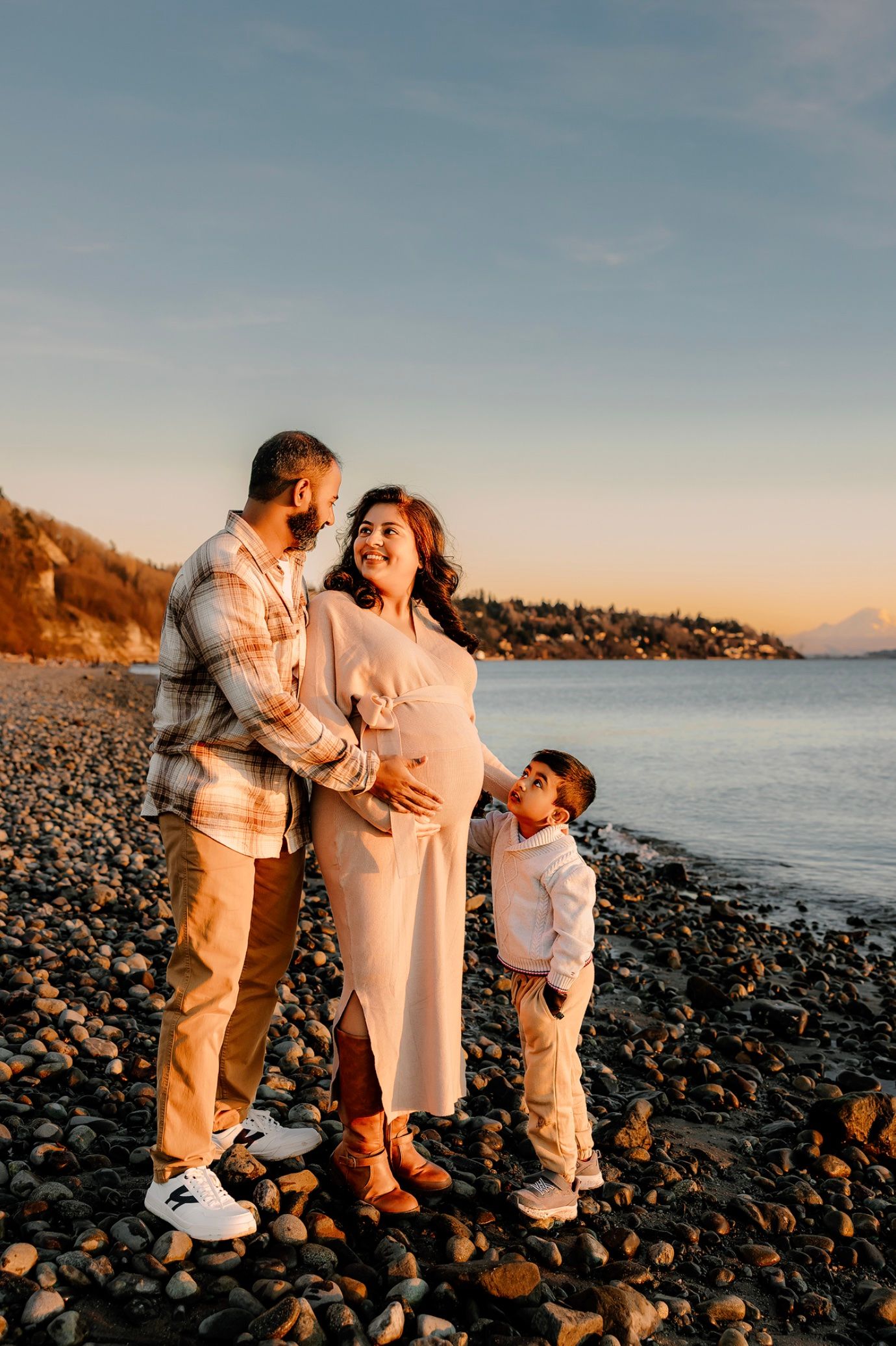A loving family shares joyful moments together on a rocky beach at sunset, dressed in coordinating light-colored outfits.