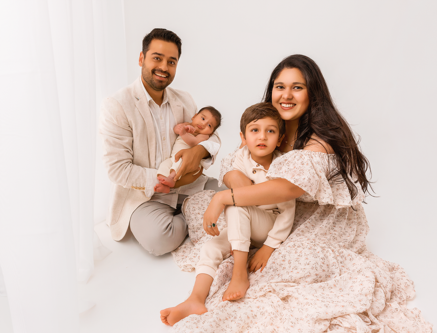 Family wearing white outfits lies together on light colored background during professional photo session.