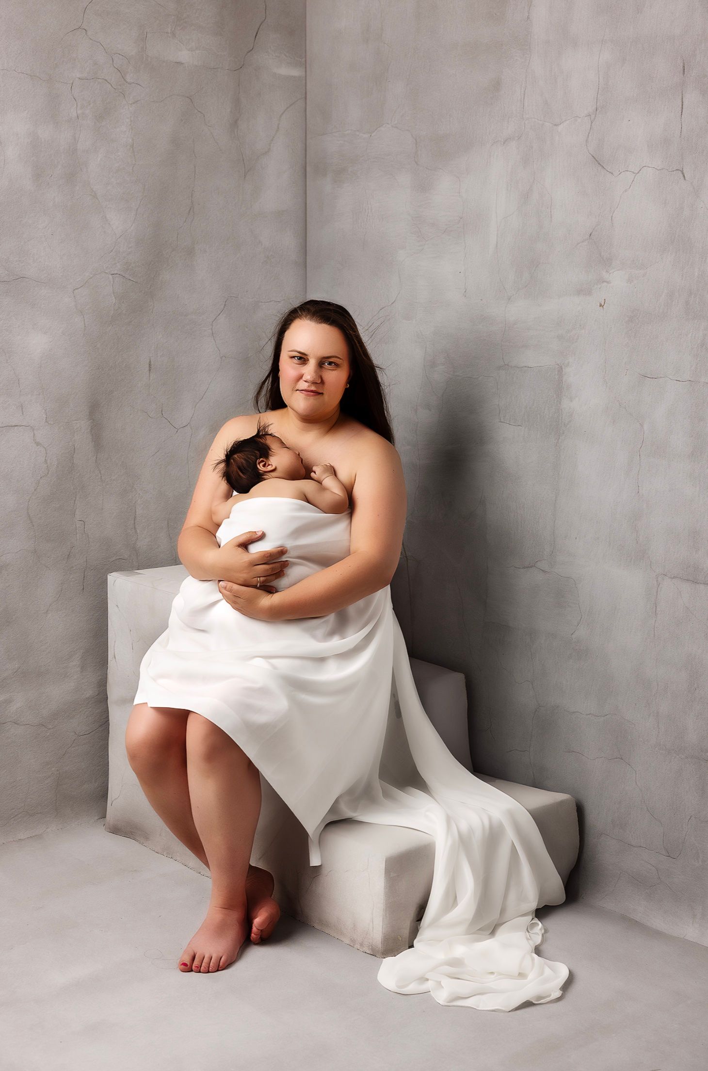 Intimate portrait session featuring parent and baby against textured grey wall.