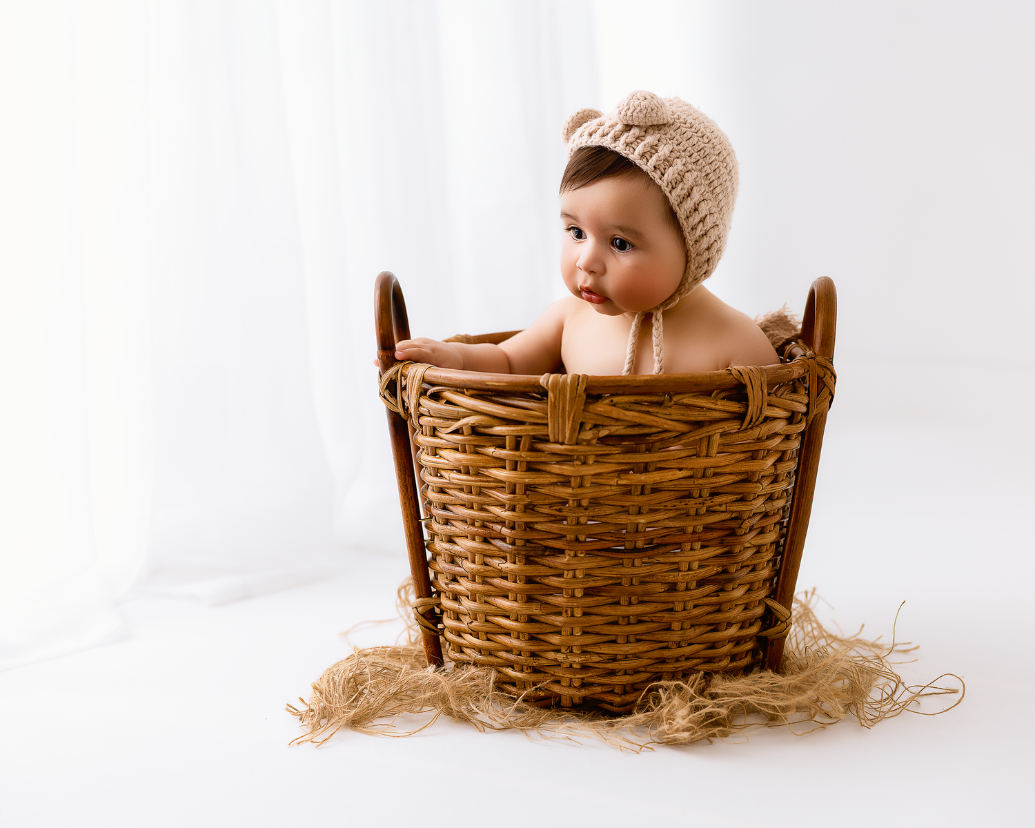 Newborn wearing knit hat rests in rustic woven basket.