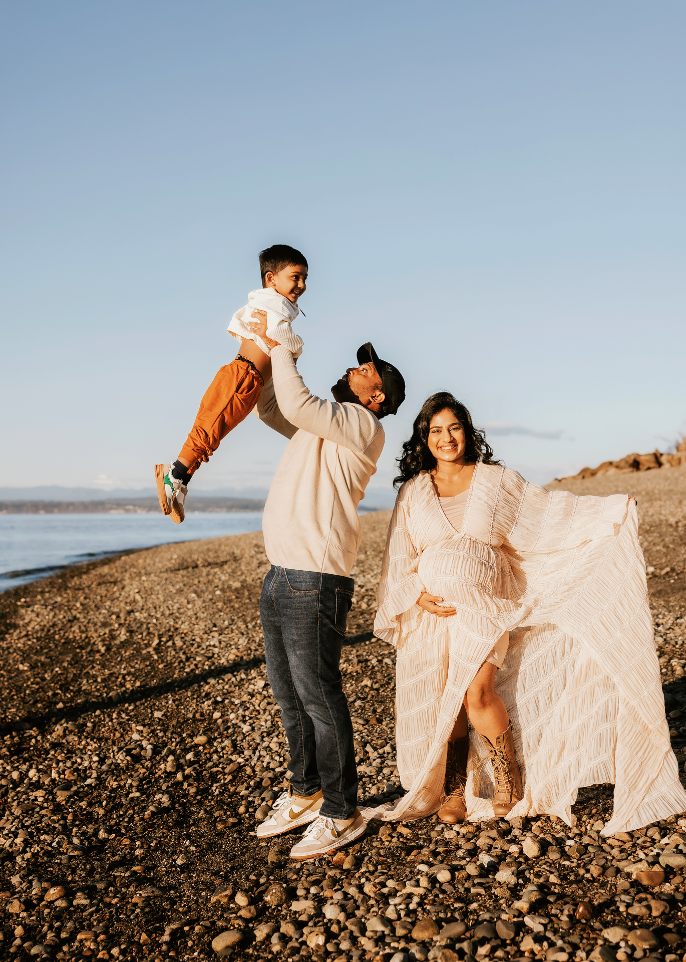 A family plays and dances together on a rocky beach at sunset, creating joyful candid moments by the water.