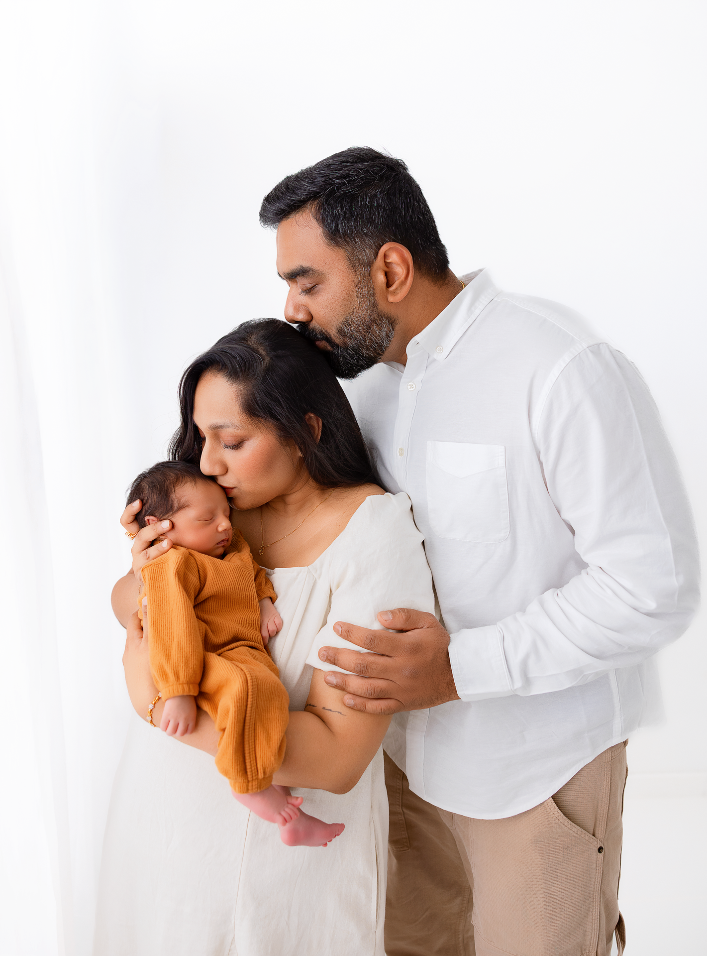 A couple in white clothing share tender moments with their baby in a series of intimate family portraits.