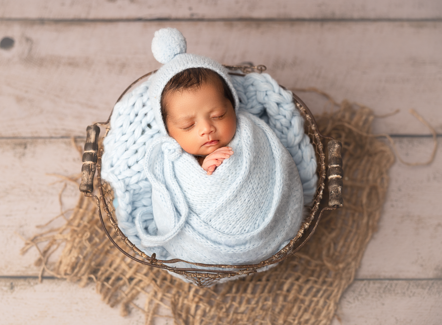 Sleeping newborn baby wrapped in soft blue blanket lying on rustic burlap fabric against wooden backdrop.