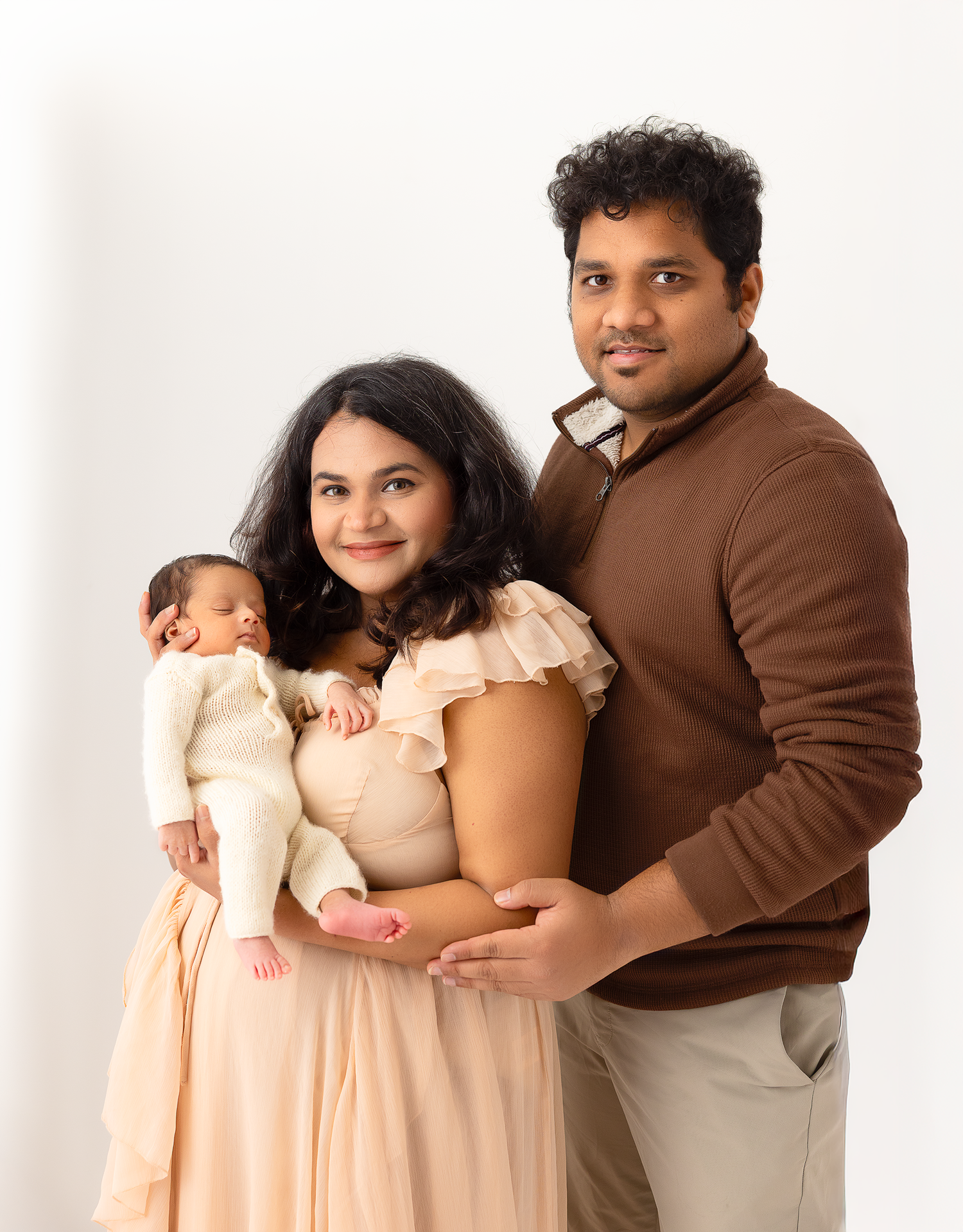 A family in coordinated brown and cream outfits poses together against a white studio backdrop.
