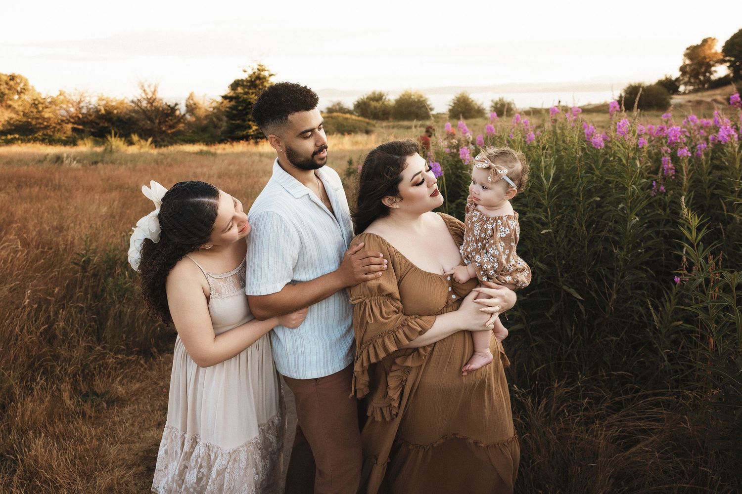 Couple and dog share tender moments in golden sunlit field with purple wildflowers at sunset.