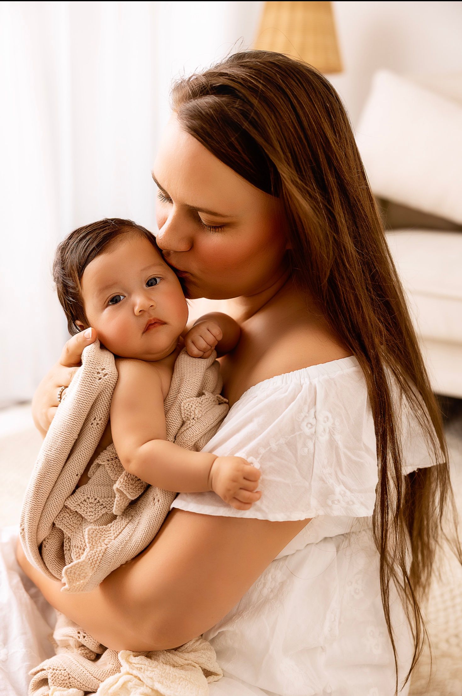 Tender moment between parent and baby in white off-shoulder dress.