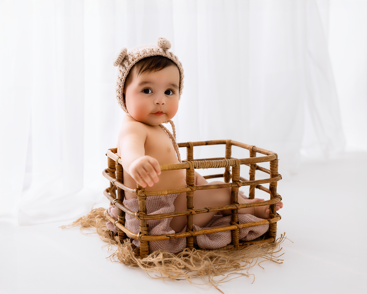 Baby sits in wooden fence prop against white backdrop during photo session.