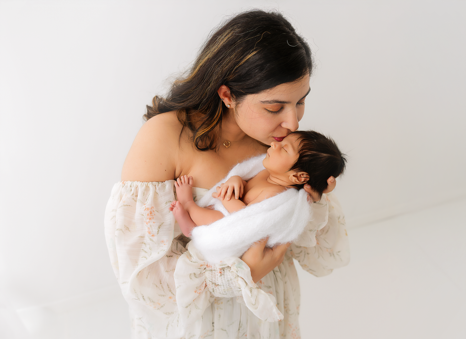 A tender moment captured in black and white as parent embraces and kisses child in white against light background.