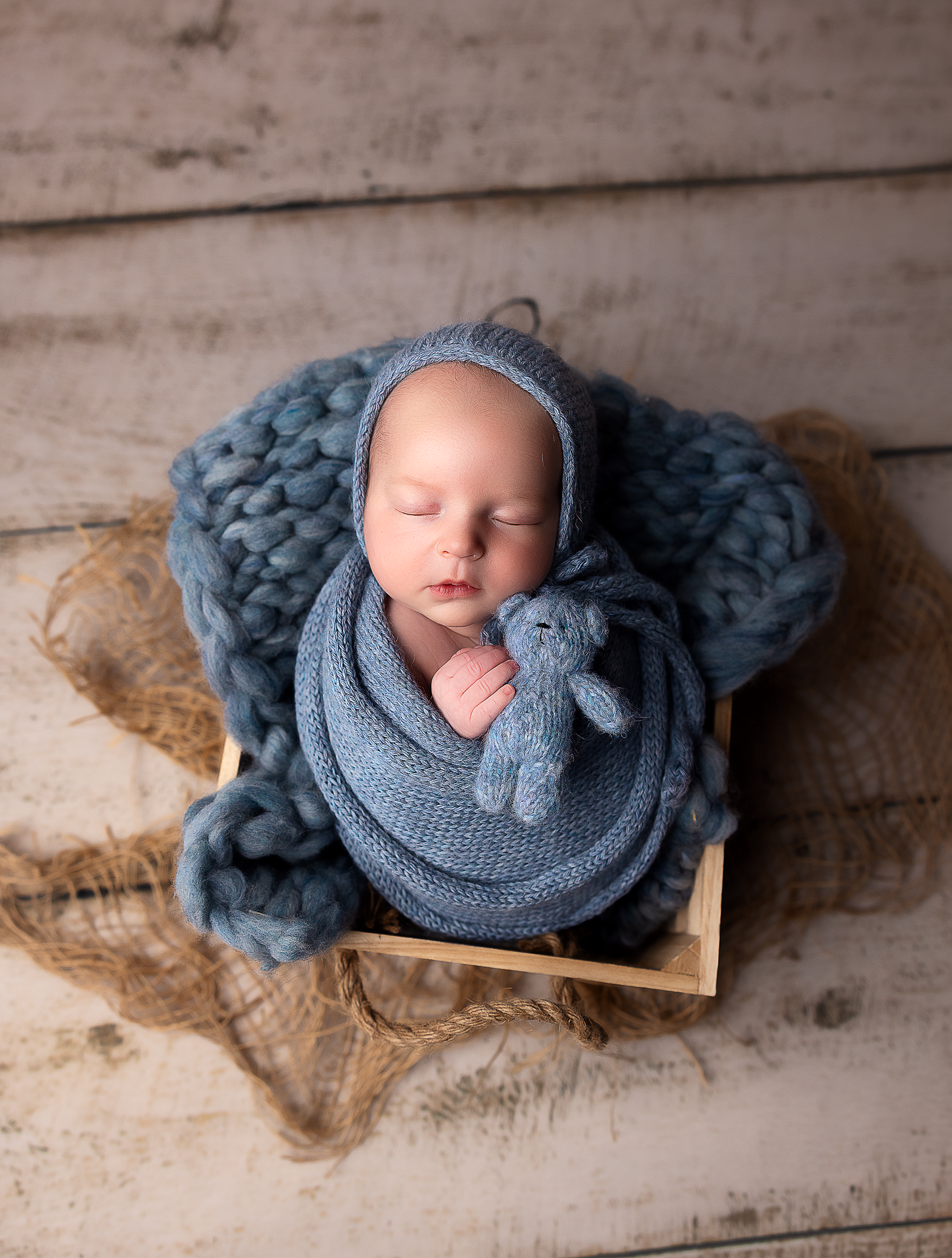 Newborn photography featuring soft blue knit wraps on rustic wooden backdrop.