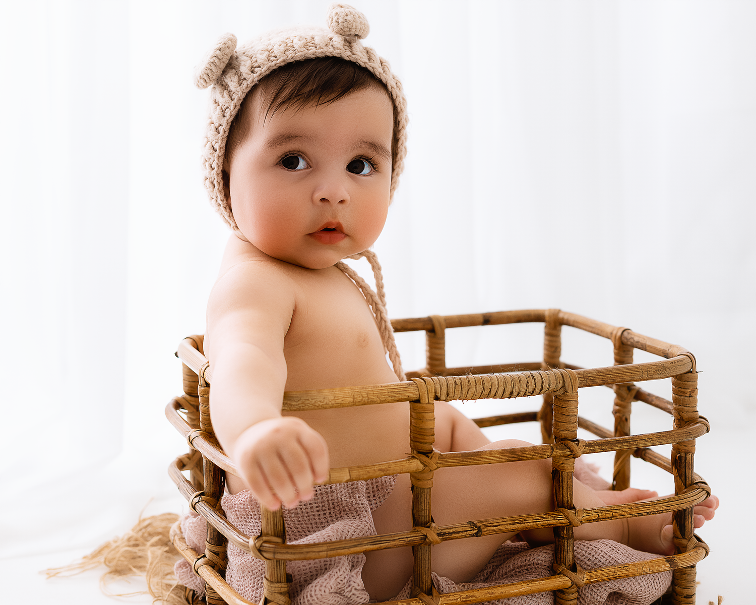 Baby wearing a knit hat sits in a wooden crate during a portrait session.