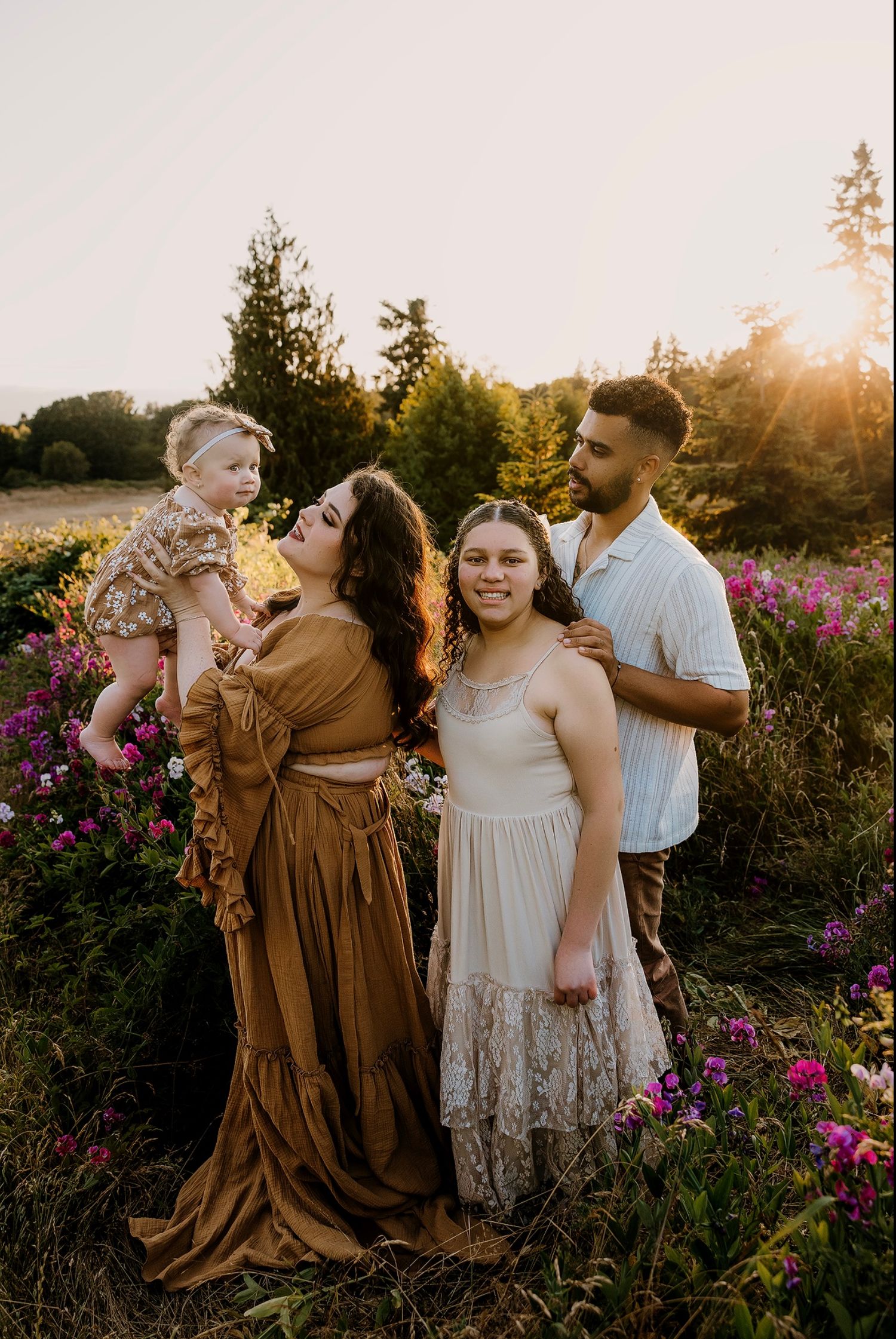 A group in brown and white dresses pose together in a wildflower field at sunset.